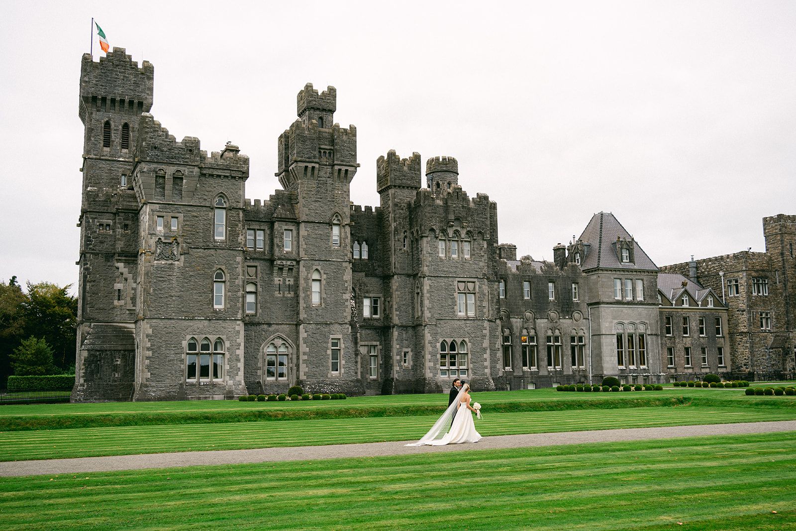 Bride and groom walking along a large estate with a castle in the background during their Irish destination wedding
