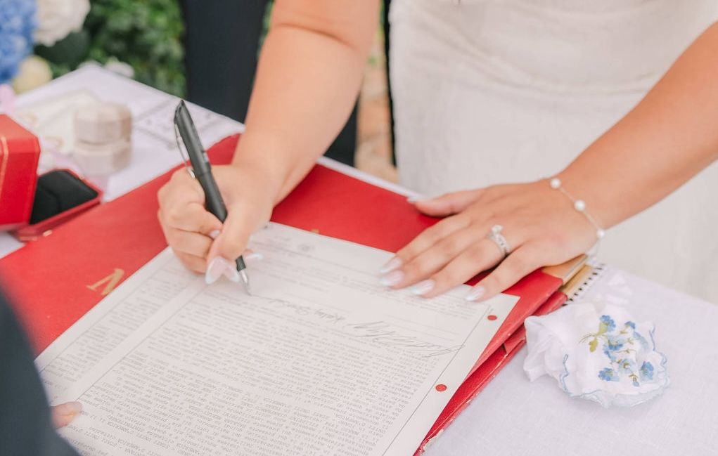 A woman’s pair of arms is shown in the photo as she signs on a white paper that lies atop a red folder