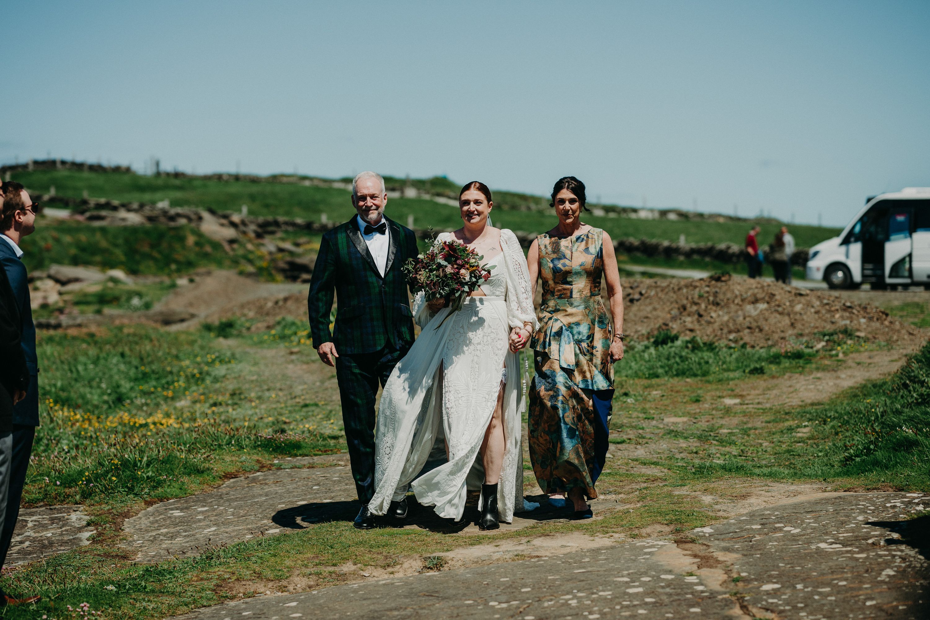 A bride walking with her father and mother on top of a grassy cliff for her small wedding in Ireland