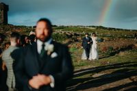 Bride walks down the clifftop aisle with her father with a rainbow in the sky