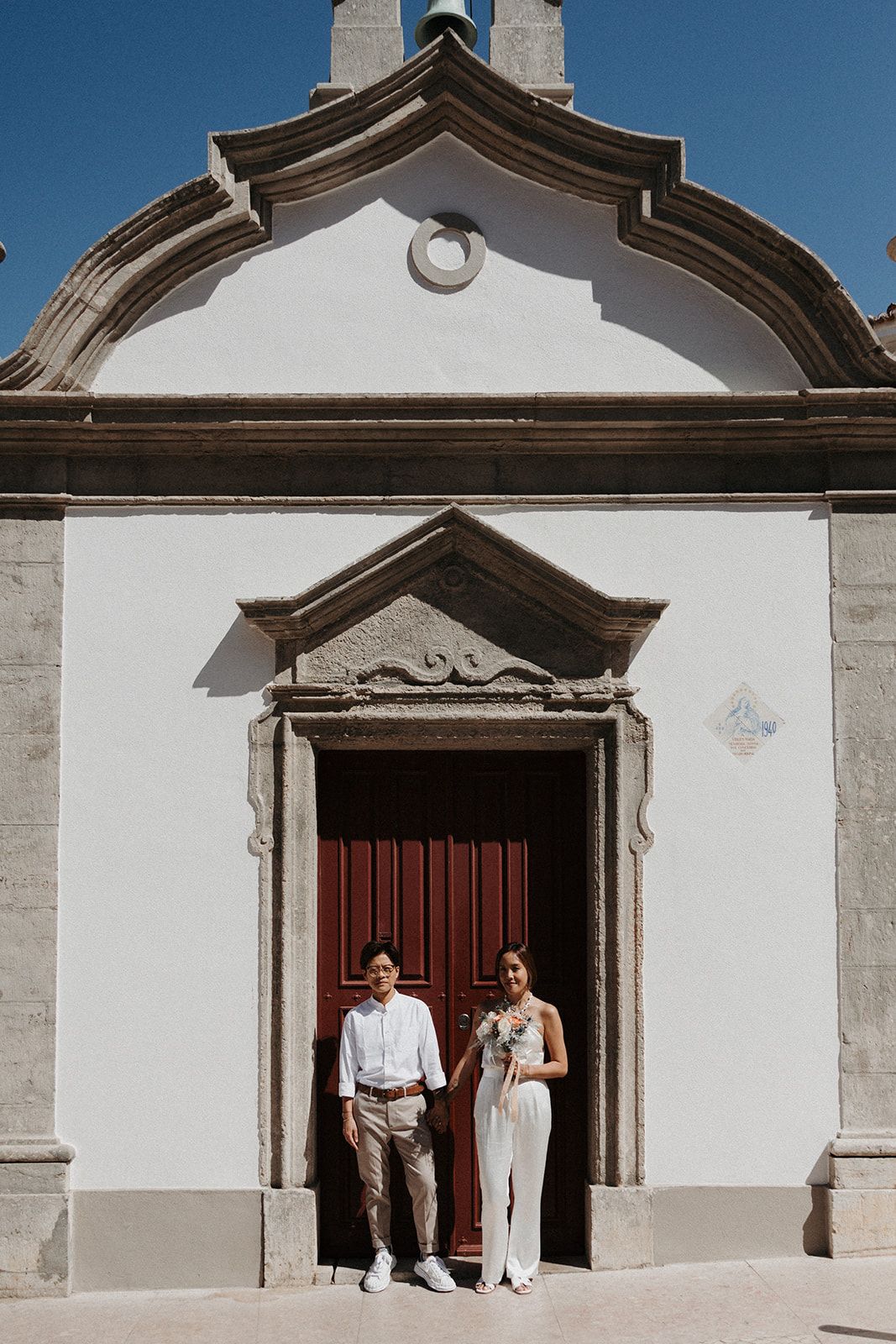 Couple in white in front of a church-like building in Lisbon during their small wedding in Portugal