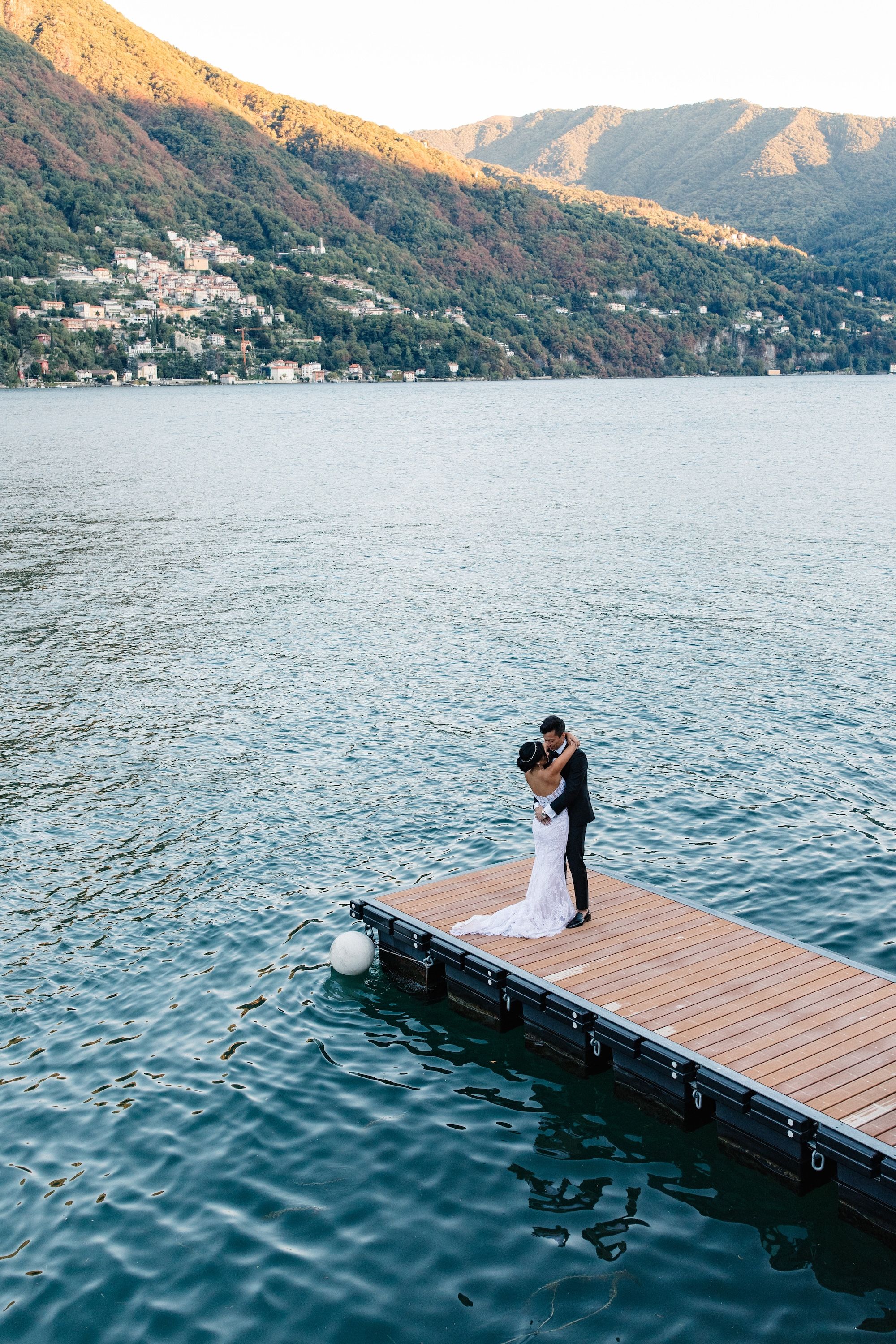 Newlyweds kissing on a wooden deck with Lake Como and Italian rolling hills in the background