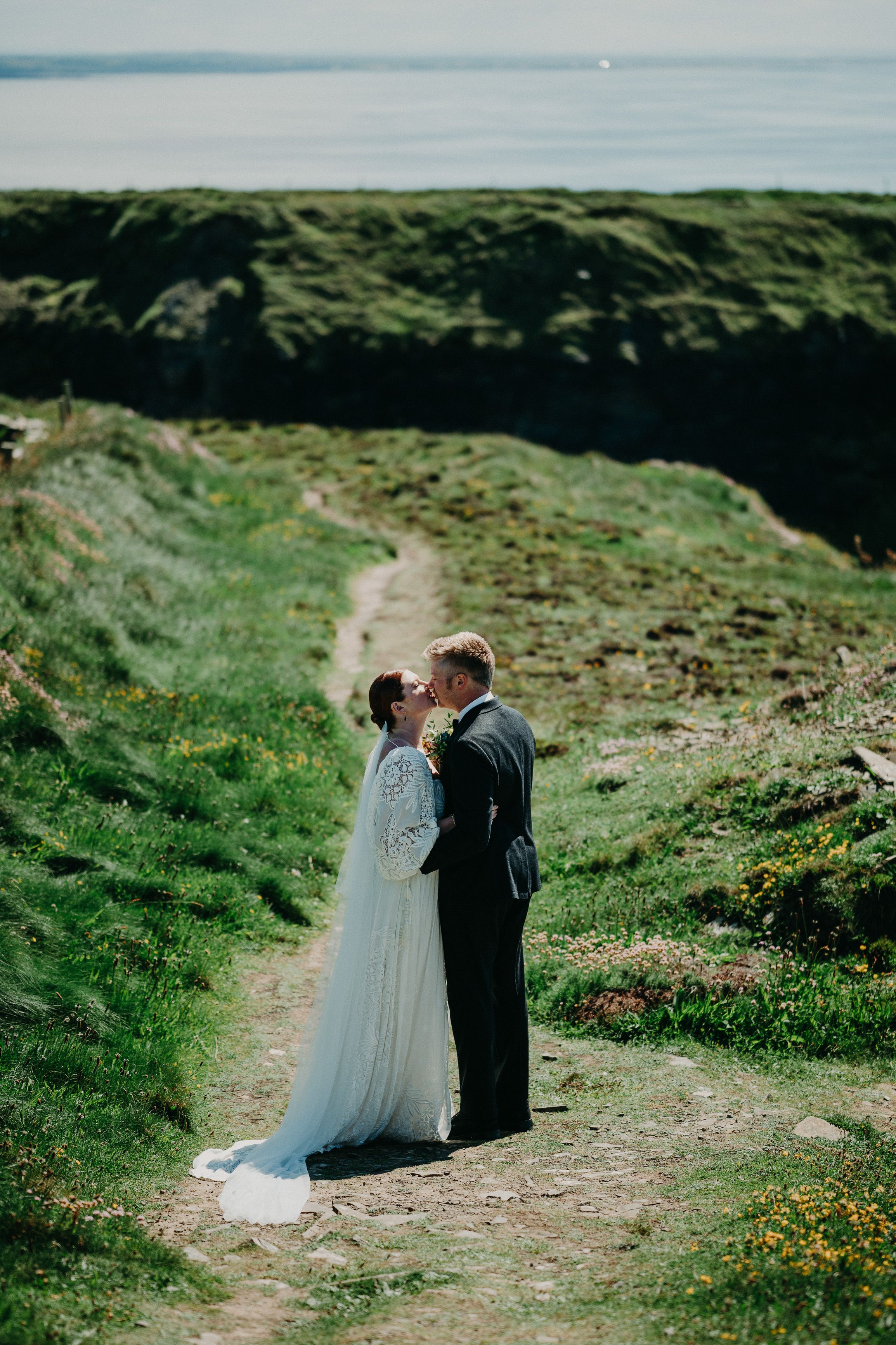 A bride and groom kissing on a grassy path on top of a cliff after their small wedding in Ireland