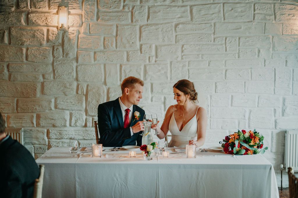 Bride and groom having a toast while seated inside a white event room during their wedding reception in Ireland