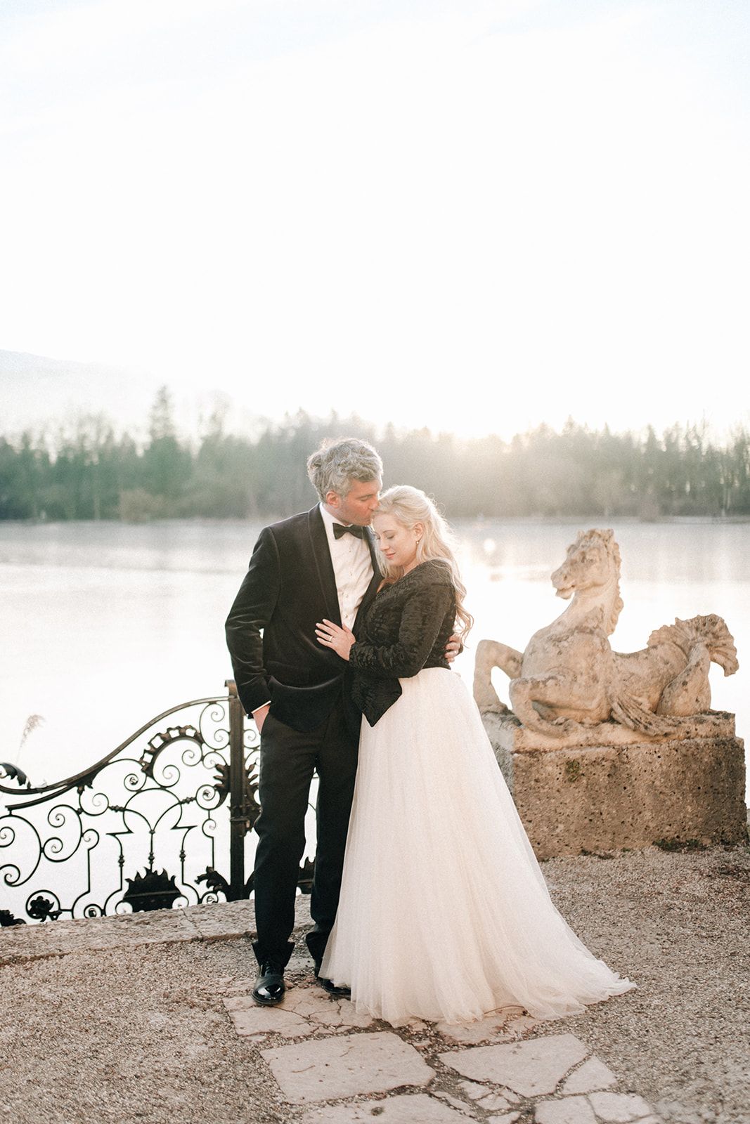 Couple embracing by stone horse statues at a Salzburg lake on a soft winter afternoon