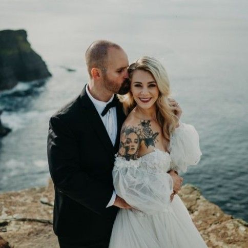 Groom kisses his bride on the temple while atop a cliff with the ocean in the background during their elopement in Ireland