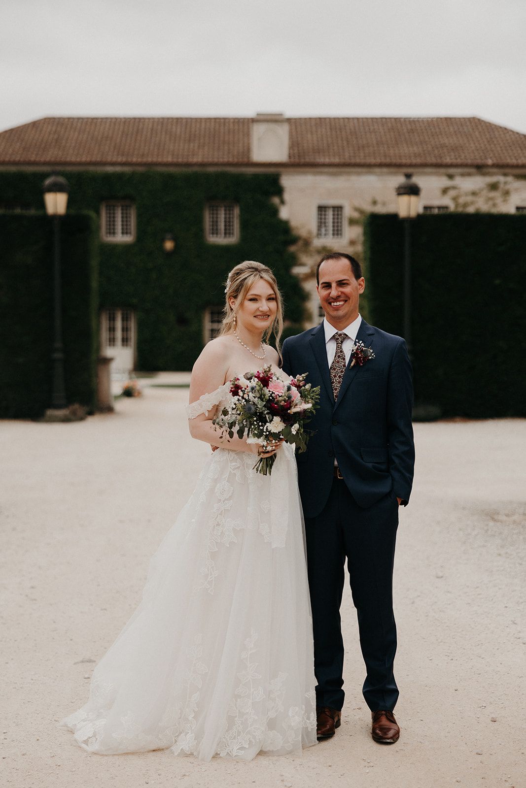 Bride and groom looking at the camera with an ivy-covered facade of a Portuguese country house in the background