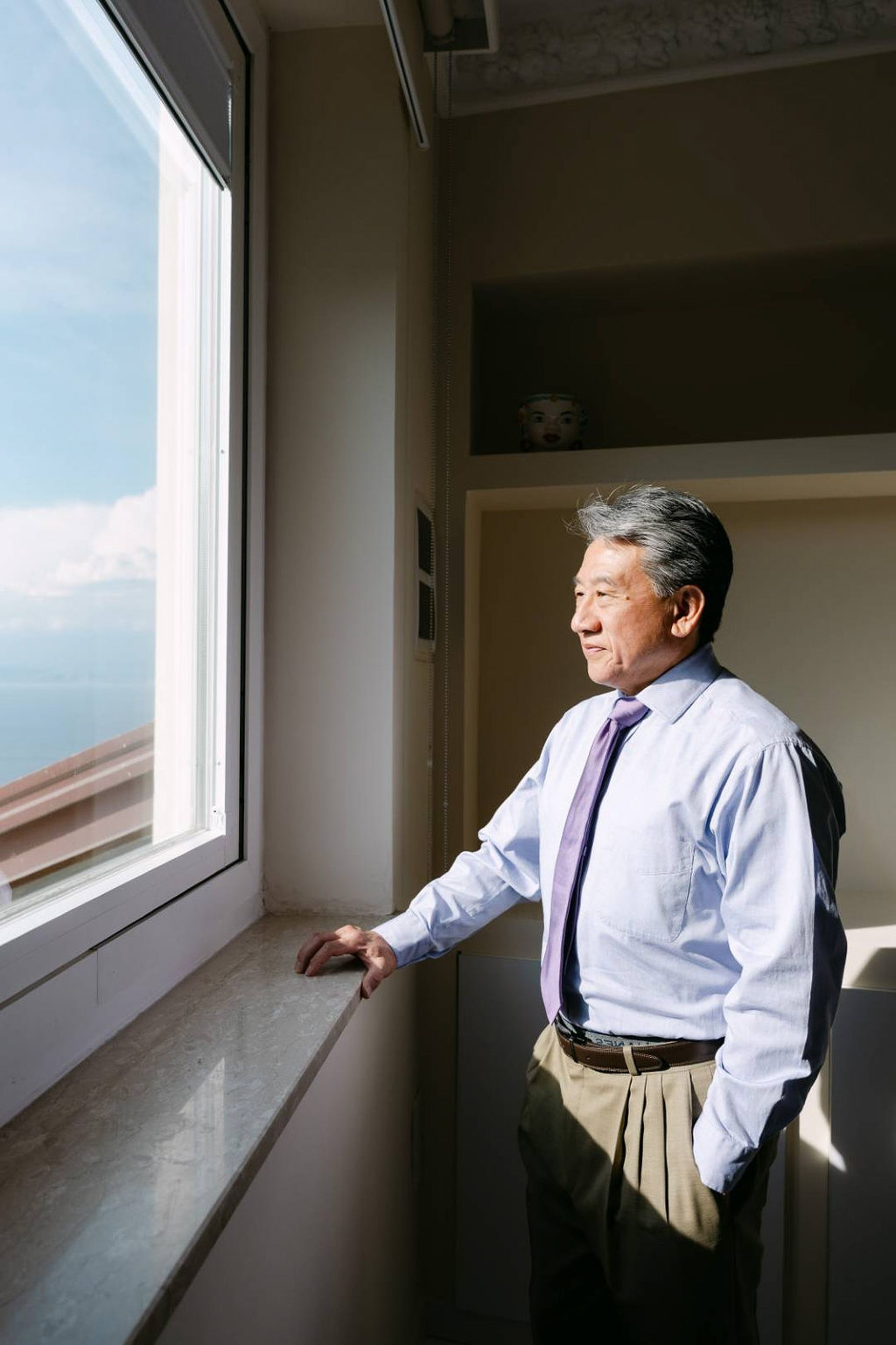Groom gazing out a window before a small wedding in Italy with coastal views and soft morning light