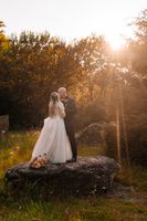 Newlyweds amidst a woodland in Ireland, kissing while standing on top of a rock, with sunset in the background