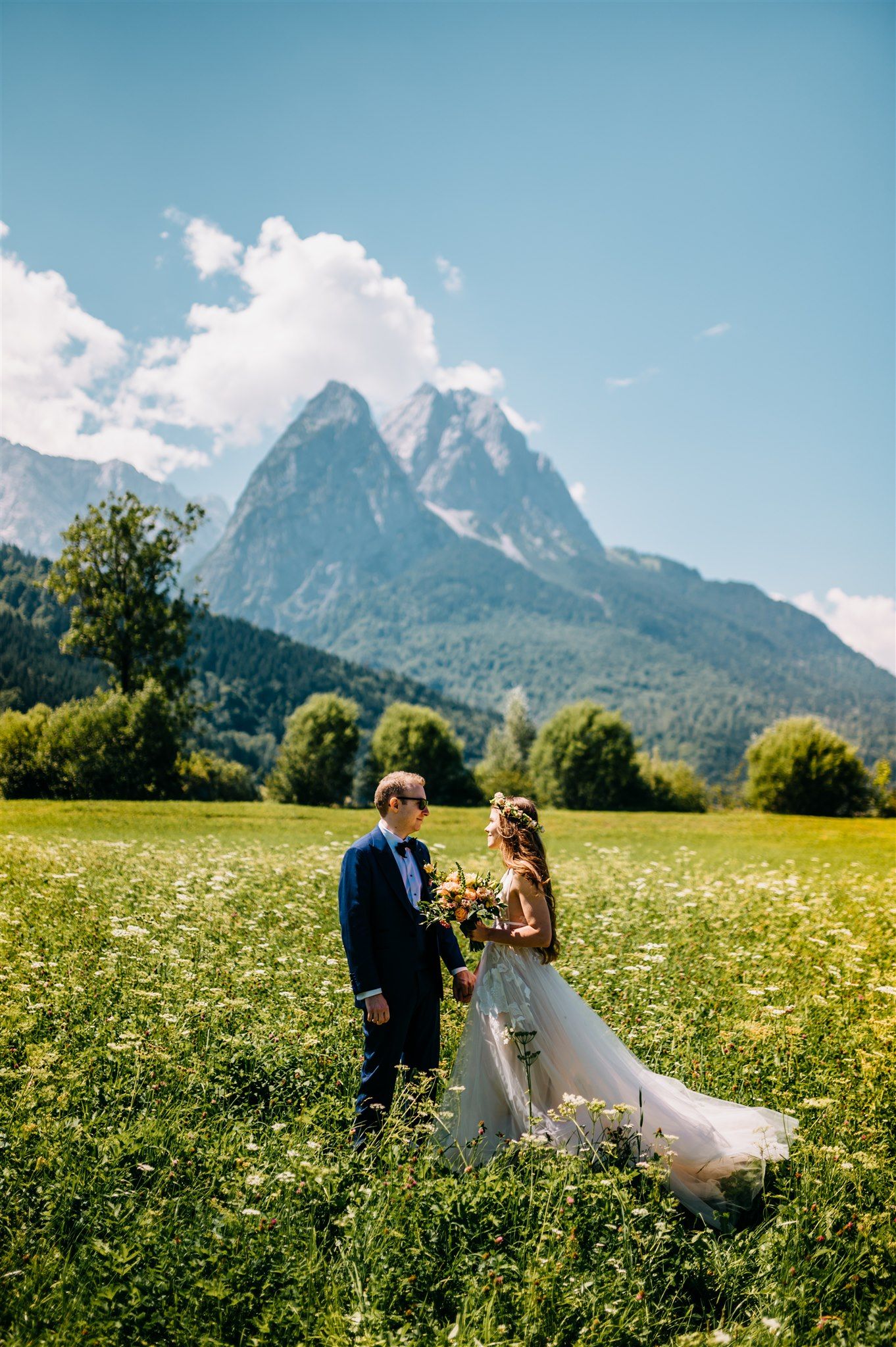 A bride and groom standing in the middle of an open field in Bavaria with a mountain behind during their small wedding in Germany