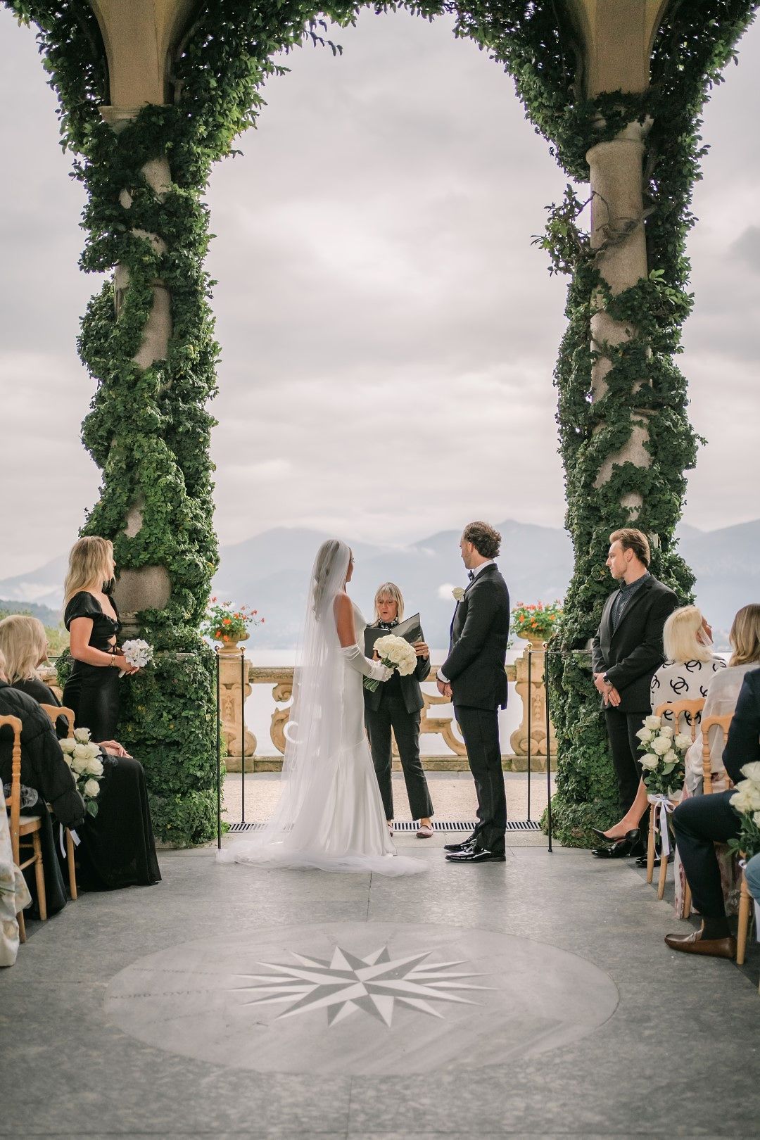 A bride and groom exchanging vows in a lakeside ceremony while friends and family look on during their small wedding in Italy