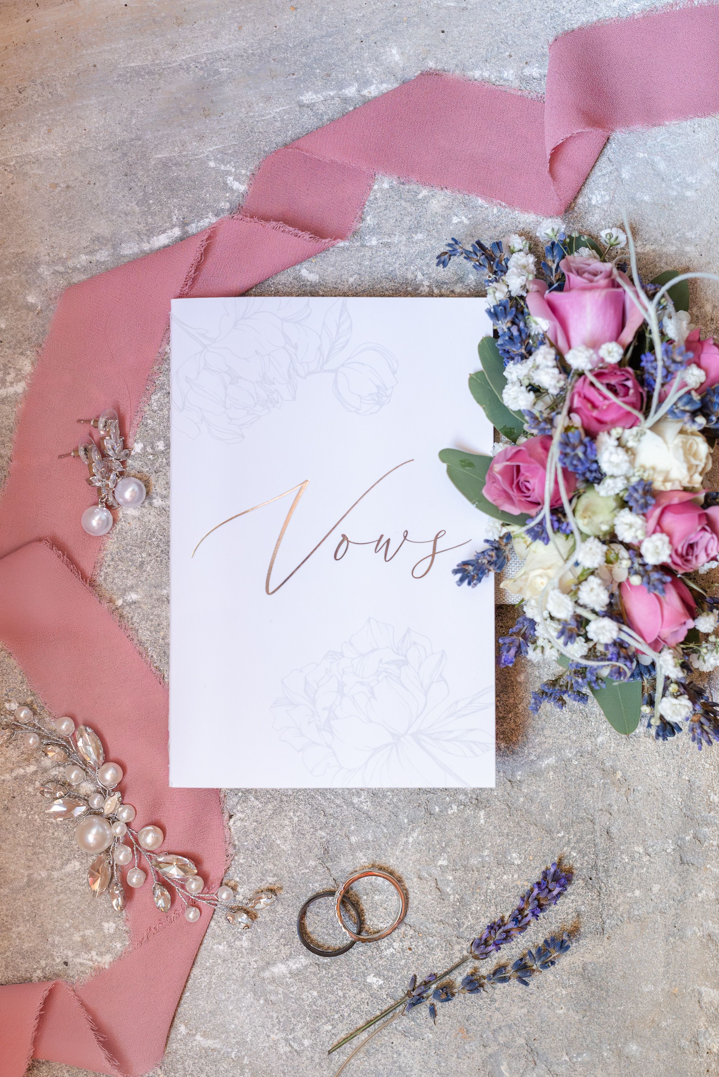 An envelop containing a couple's vows surrounded by rings, jewelry, and flowers before an intimate wedding in France