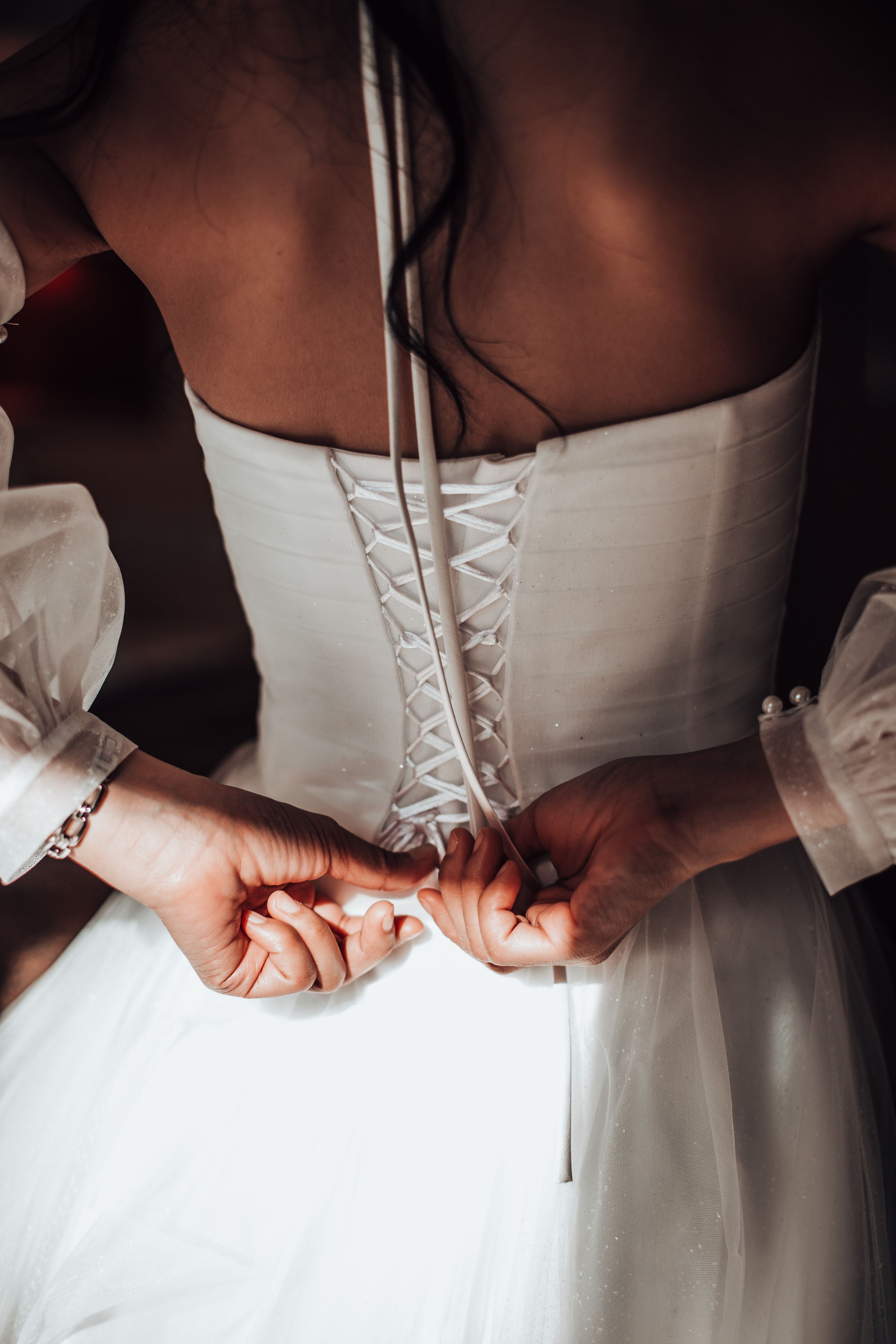 Hands lacing the back of the bride's corset wedding dress