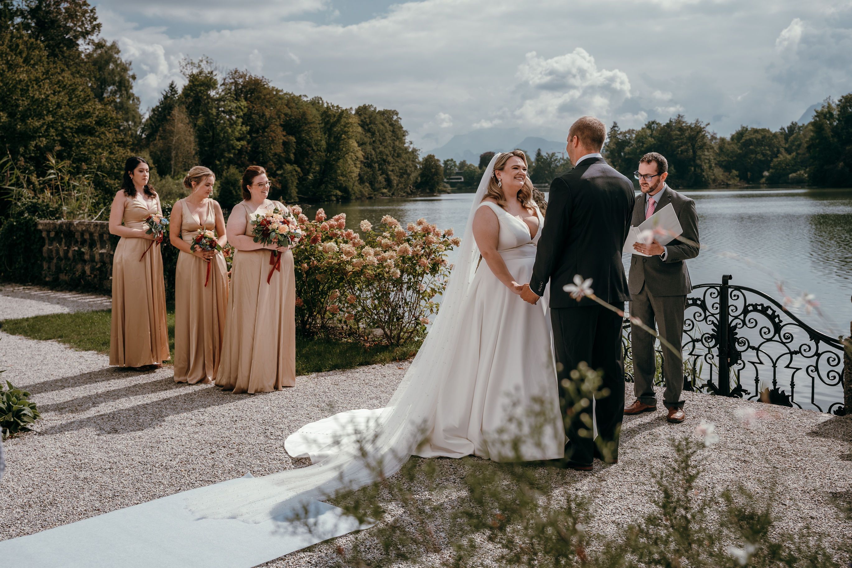Couple saying their vows by a lake in early autumn, bridesmaids in gold dresses beside them