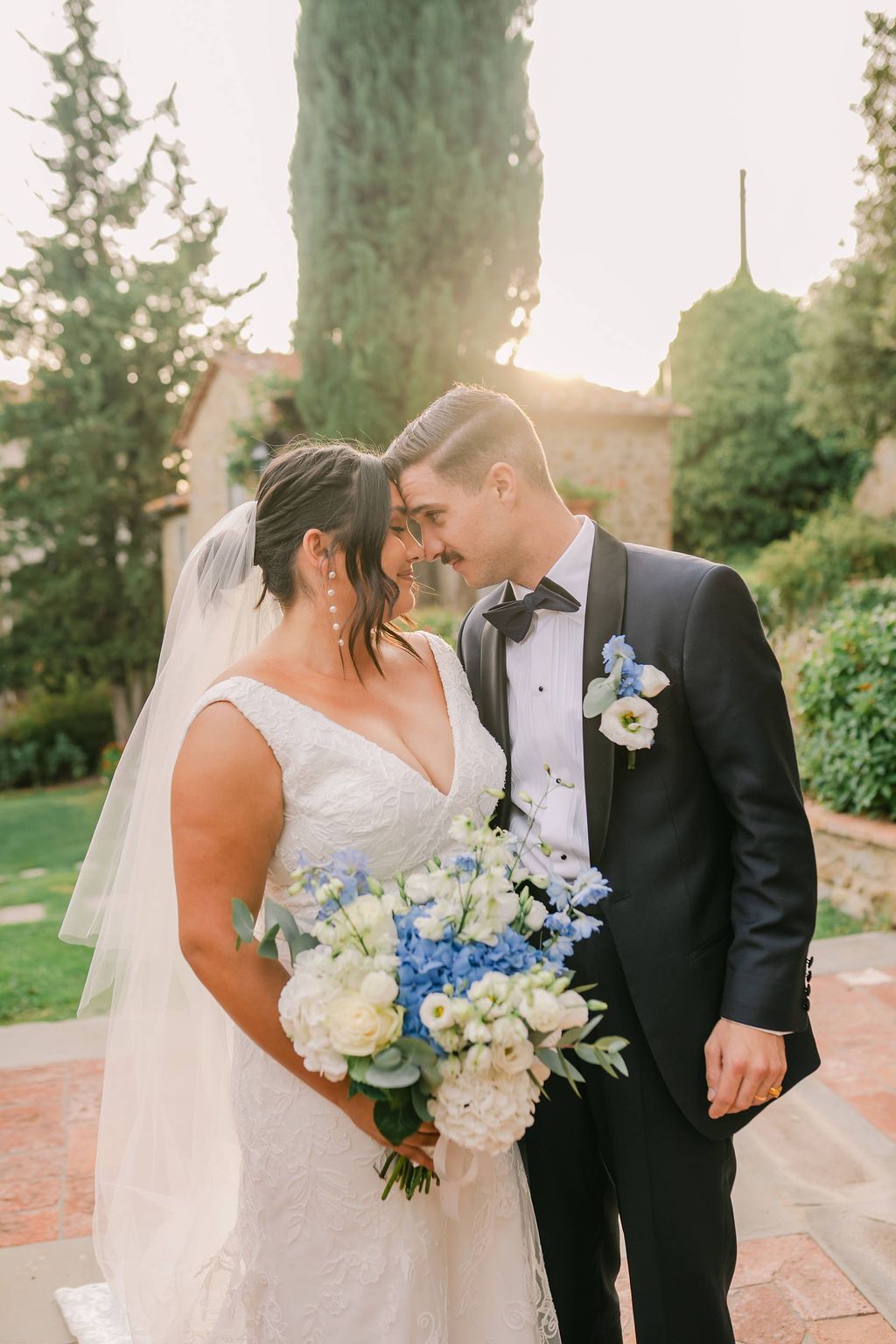 Romantic photo of newlyweds with heads close to each other and Italian greenery and the sunset in the background