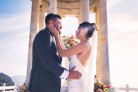 Bride and groom looking at each other with the sun and a stone gazebo behind when they eloped in Spain atop a Mallorcan cliff