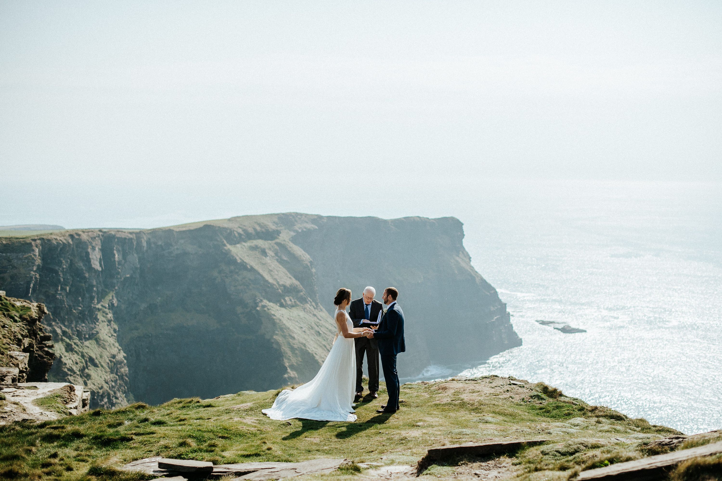 Bride and groom holding hands with ocean cliffs in the background at an intimate wedding in Europe