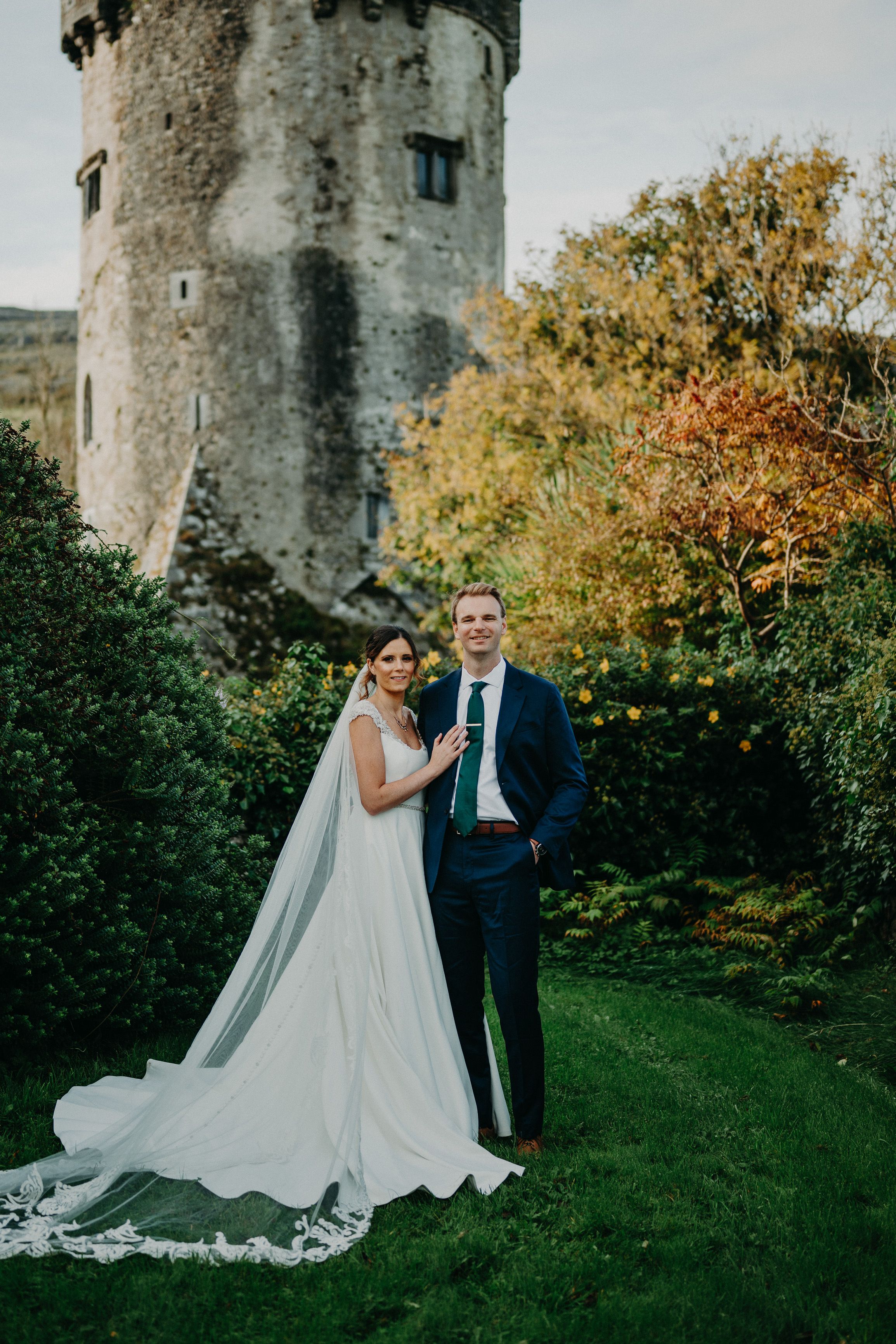 Small wedding in Ireland bride and groom posing in the garden with a castle tower backdrop in autumn
