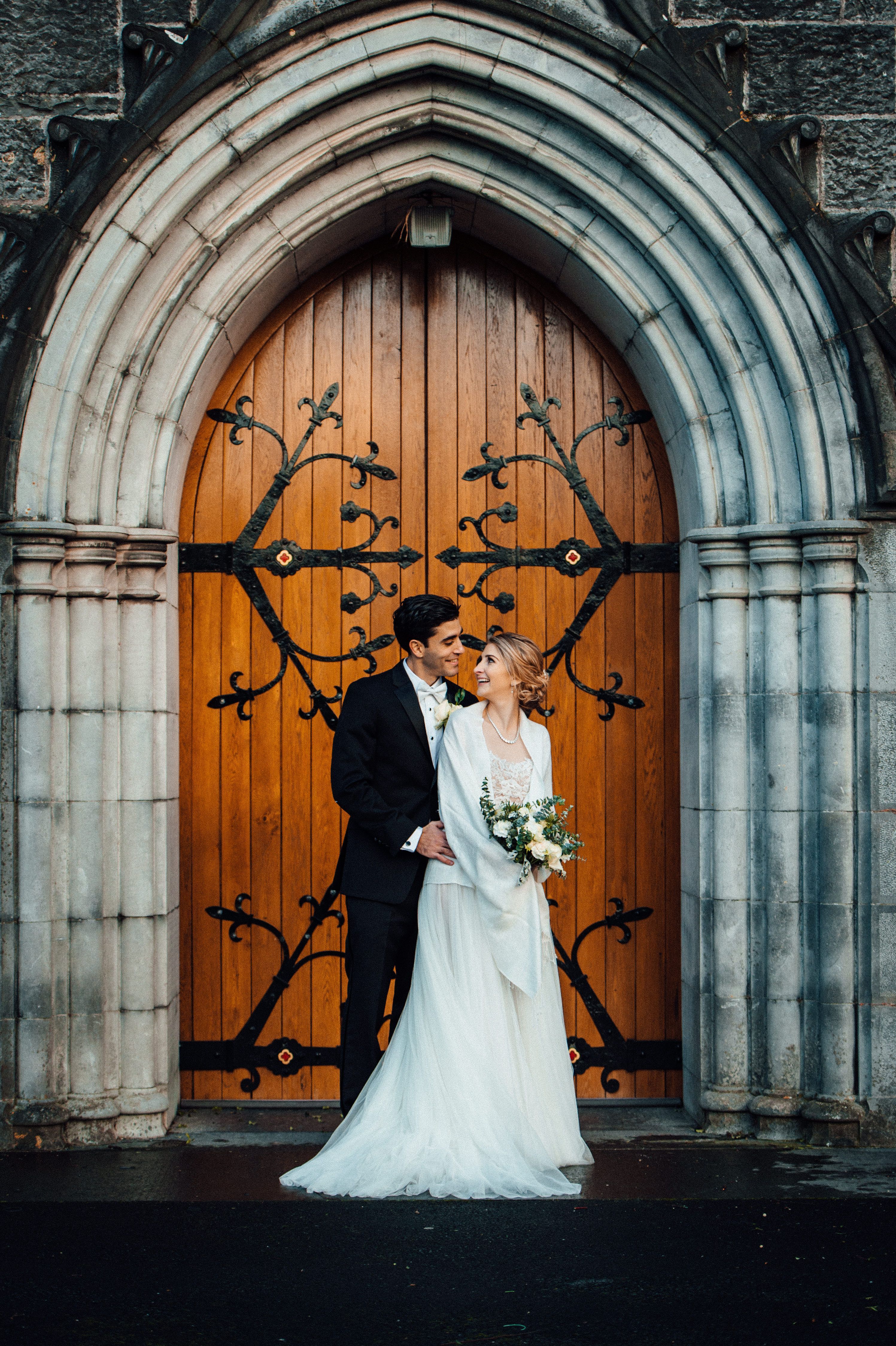 Newlyweds in a photoshoot in front of a wooden door of a chapel after the ceremony of their destination wedding in Ireland
