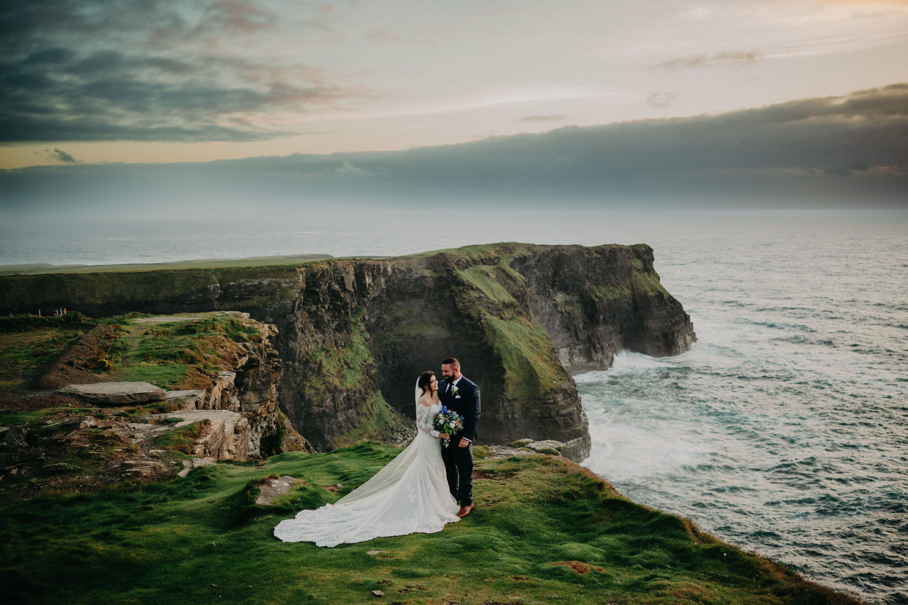 Newlyweds on top of a cliff in Ireland for a photoshoot overlooking the ocean