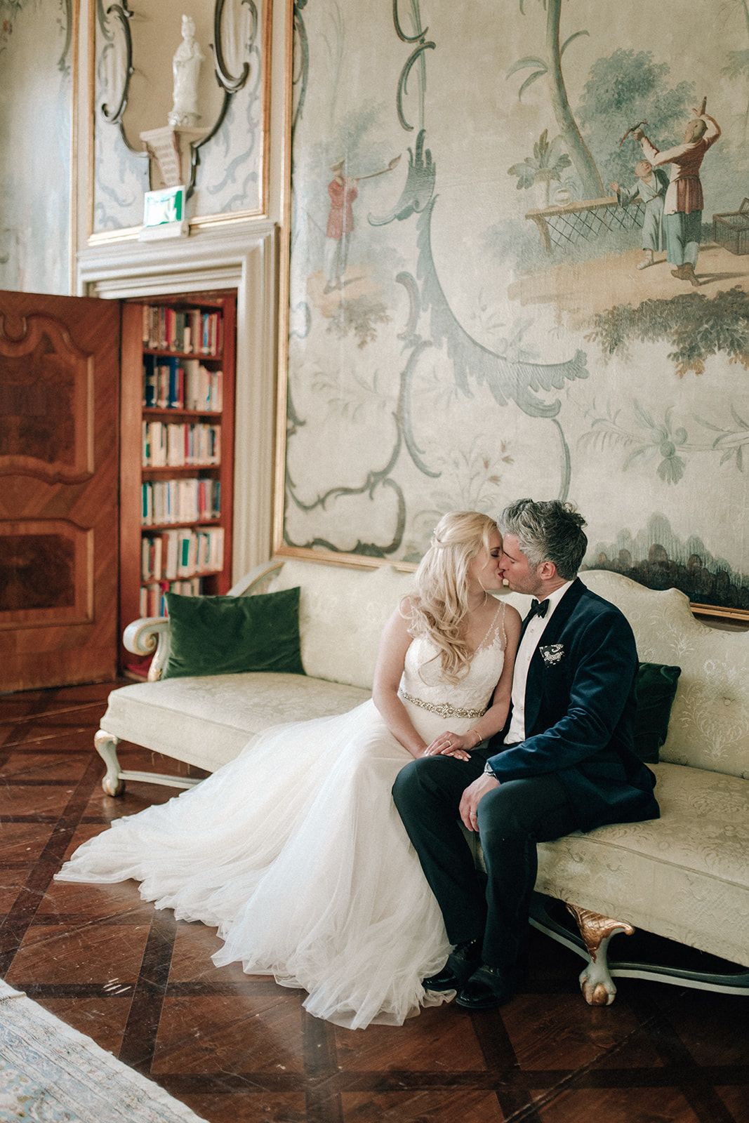 Newlyweds kissing on an antique sofa in a frescoed salon of an Austrian palace