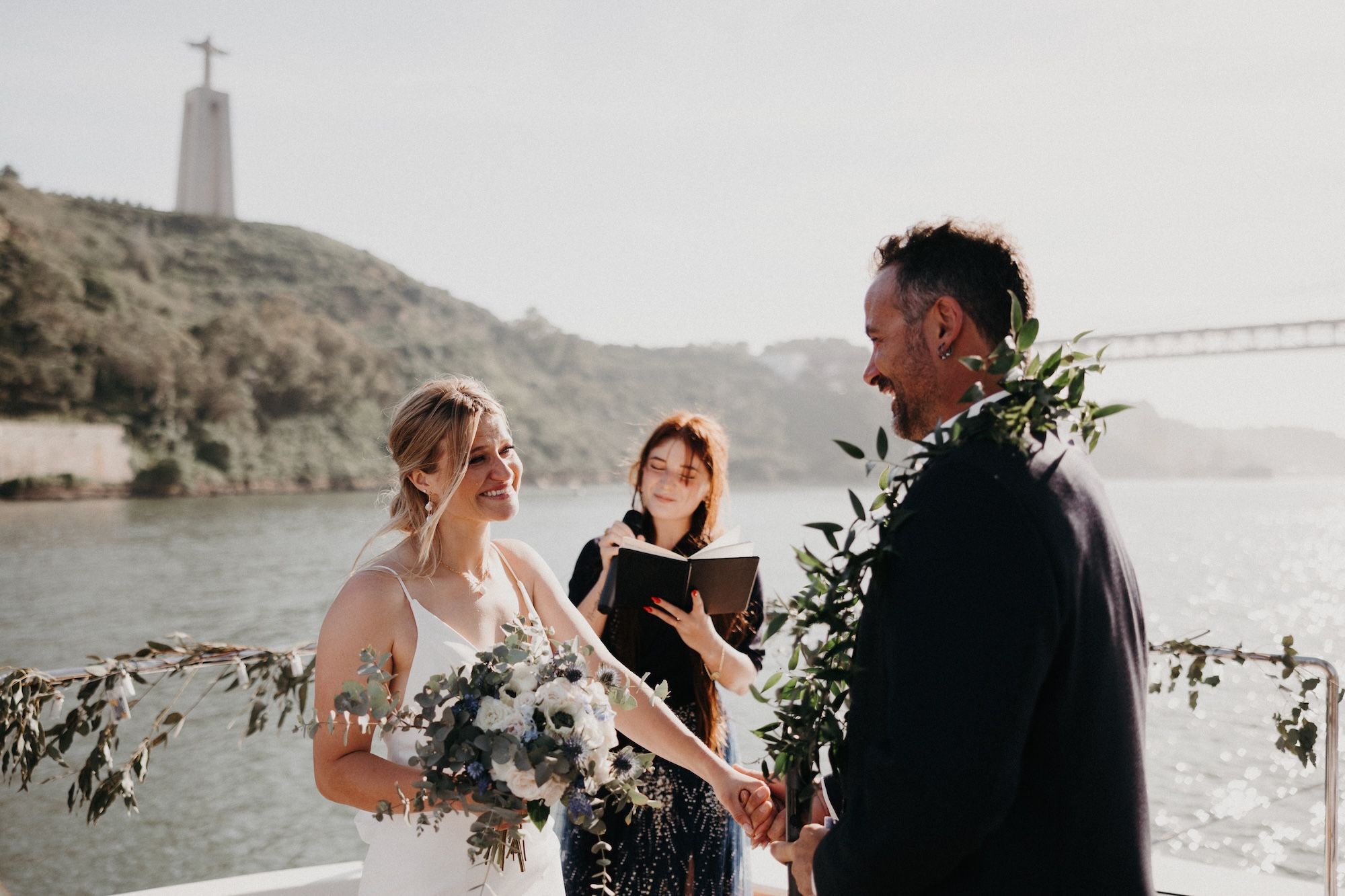 Bride and groom with celebrant, having a ceremony on a boat sailing in Tagus River during a destination wedding in Portugal