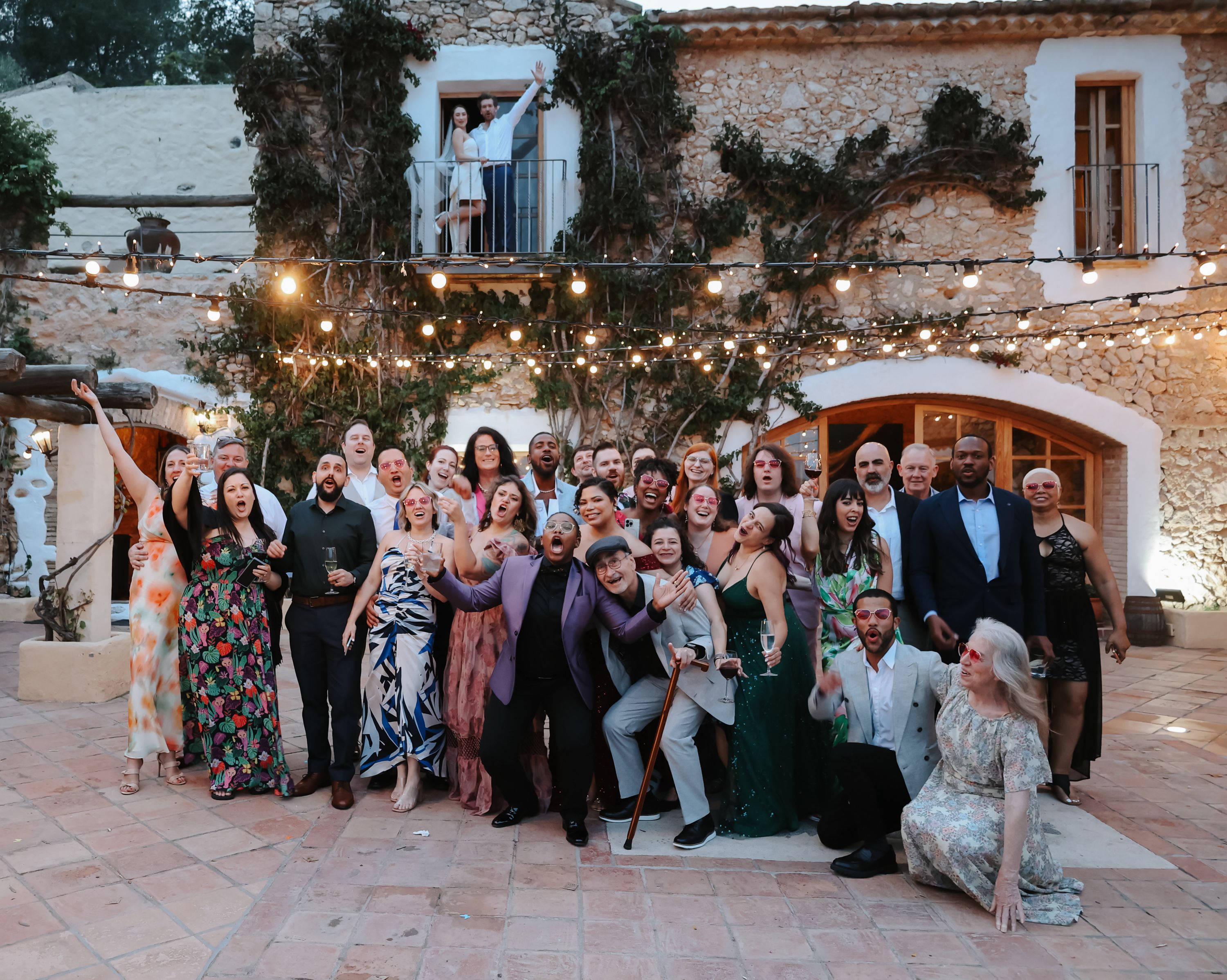 Bride and groom in the balcony with their guests for their intimate wedding in Spain with fairy lights on top of them