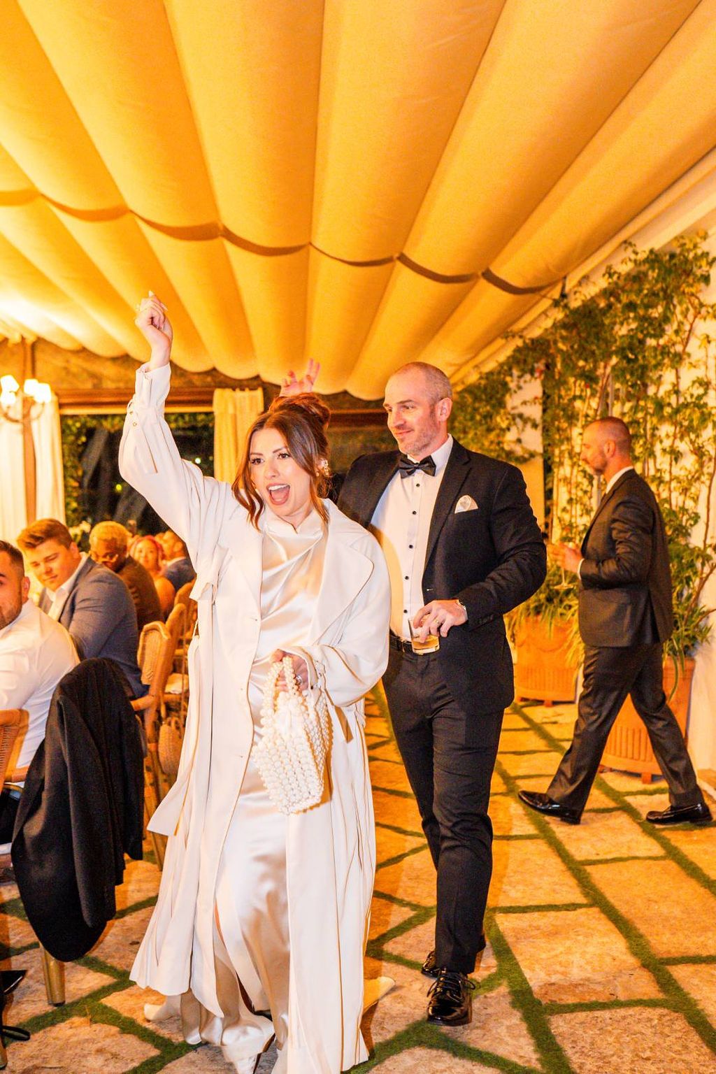 Bride raises her hand in celebration as she walks with her groom to the party area of their vow renewal in Italy
