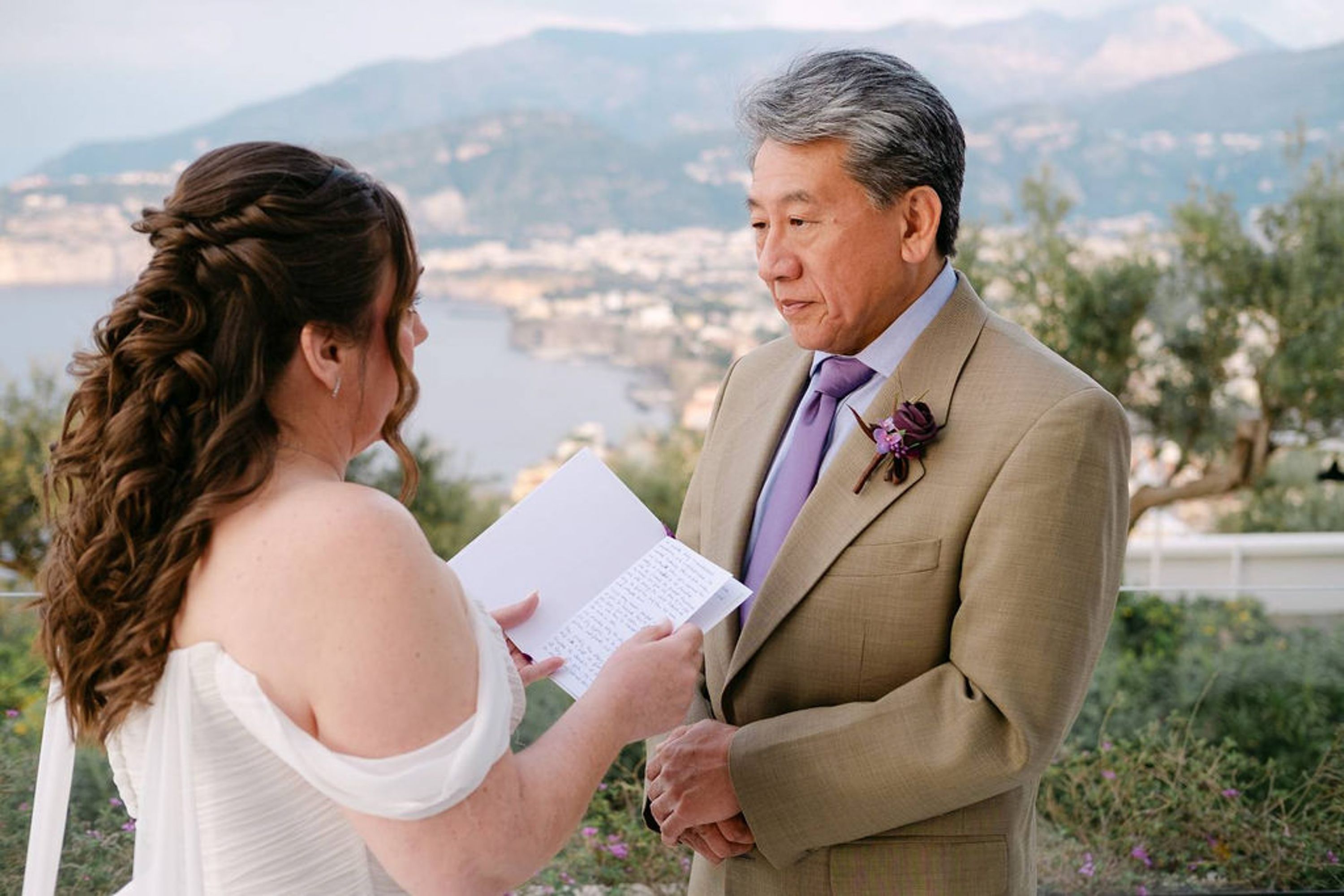 Groom listens attentively as bride reads vows overlooking the coast at an intimate wedding in Italy