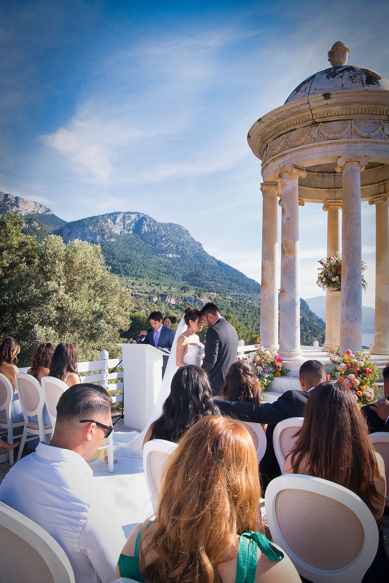 Bride and groom in front of a white stone gazebo, having a ceremony during their destination wedding Spain
