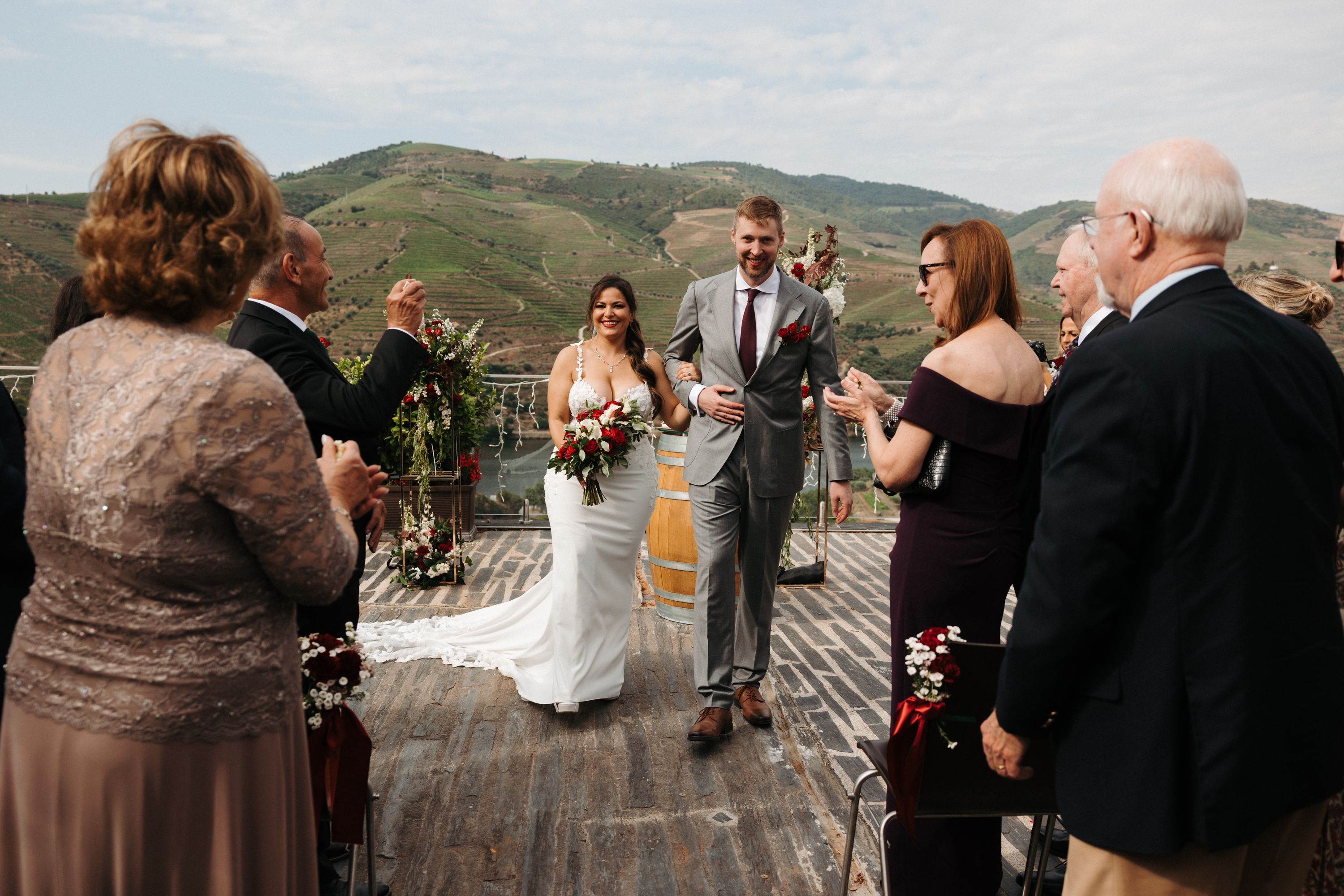 Bride and groom walking down the aisle, with a mountain panorama in the background, while their guests cheer them