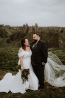 Newlyweds on the cliffs of Antrim with the castle ruin in the backdrop during the photoshoot of their elopement in Ireland