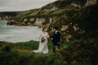 Newlyweds on top of a cliff in Antrim during the photoshoot of their destination wedding in Ireland, with the Atlantic Ocean and cliffs in the background.