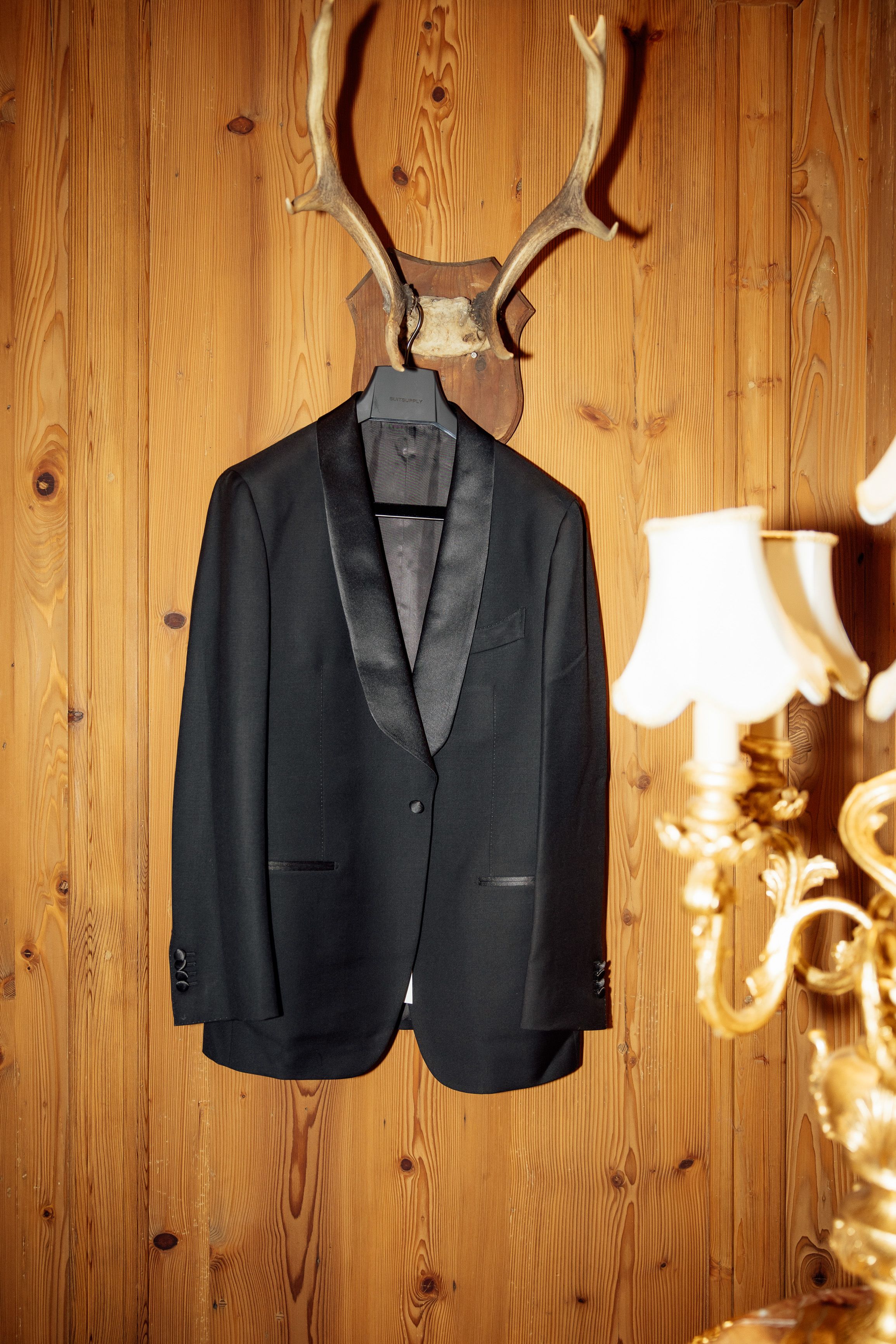 Black tuxedo hanging against rustic wooden walls before an intimate wedding in Austria