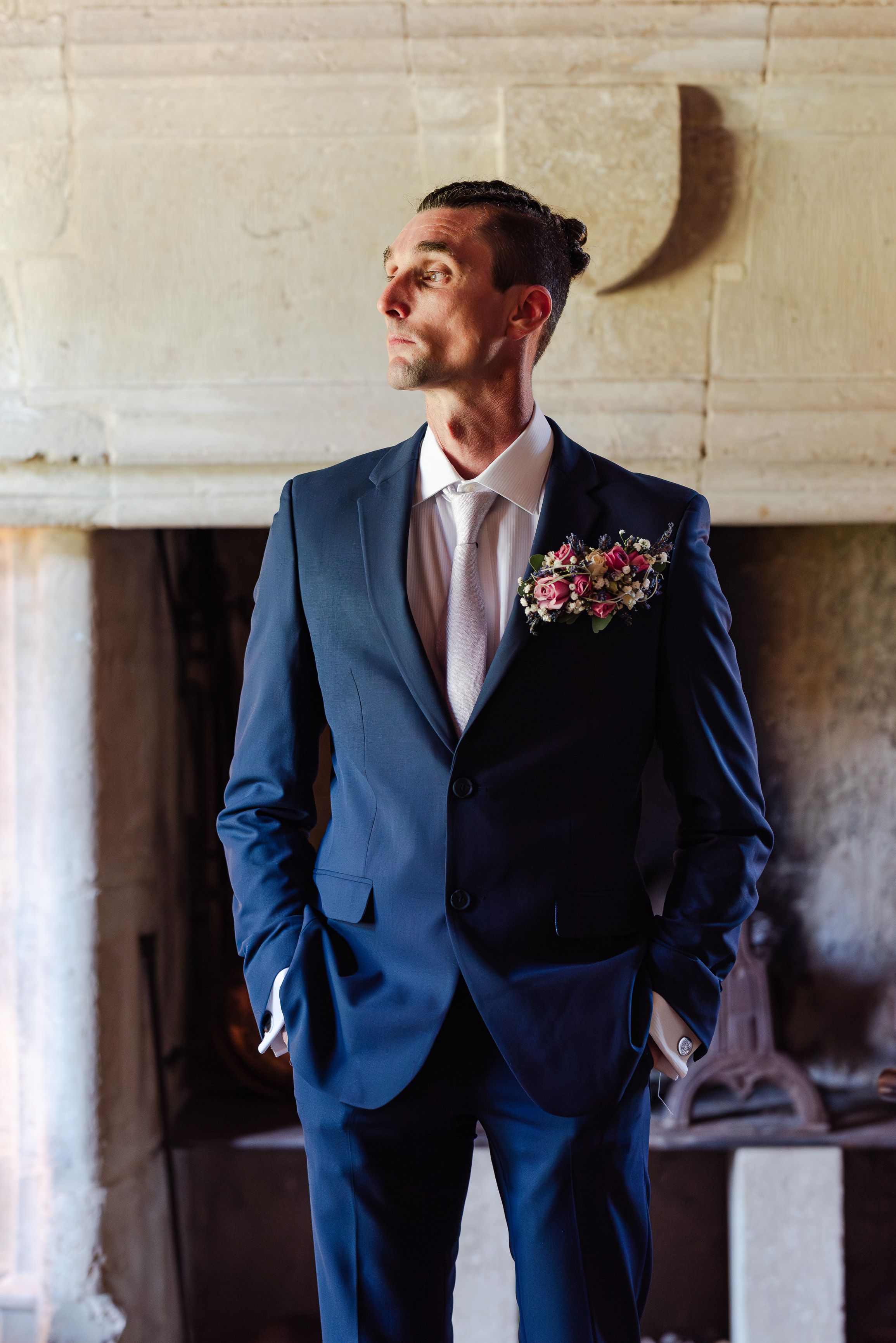 Groom portrait in a blue suit beside a stone fireplace during an intimate wedding in France