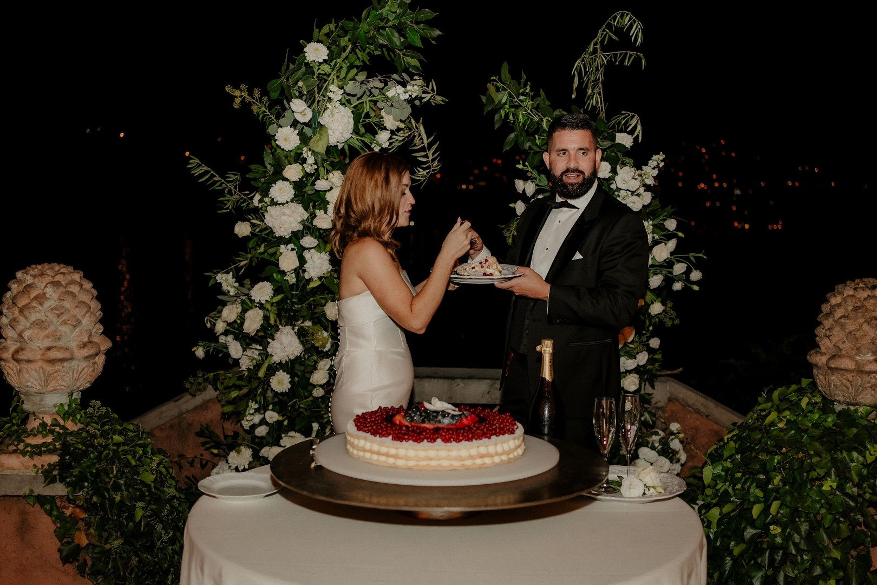 Newlyweds share wedding cake beneath floral arrangements during an intimate wedding in Italy celebration