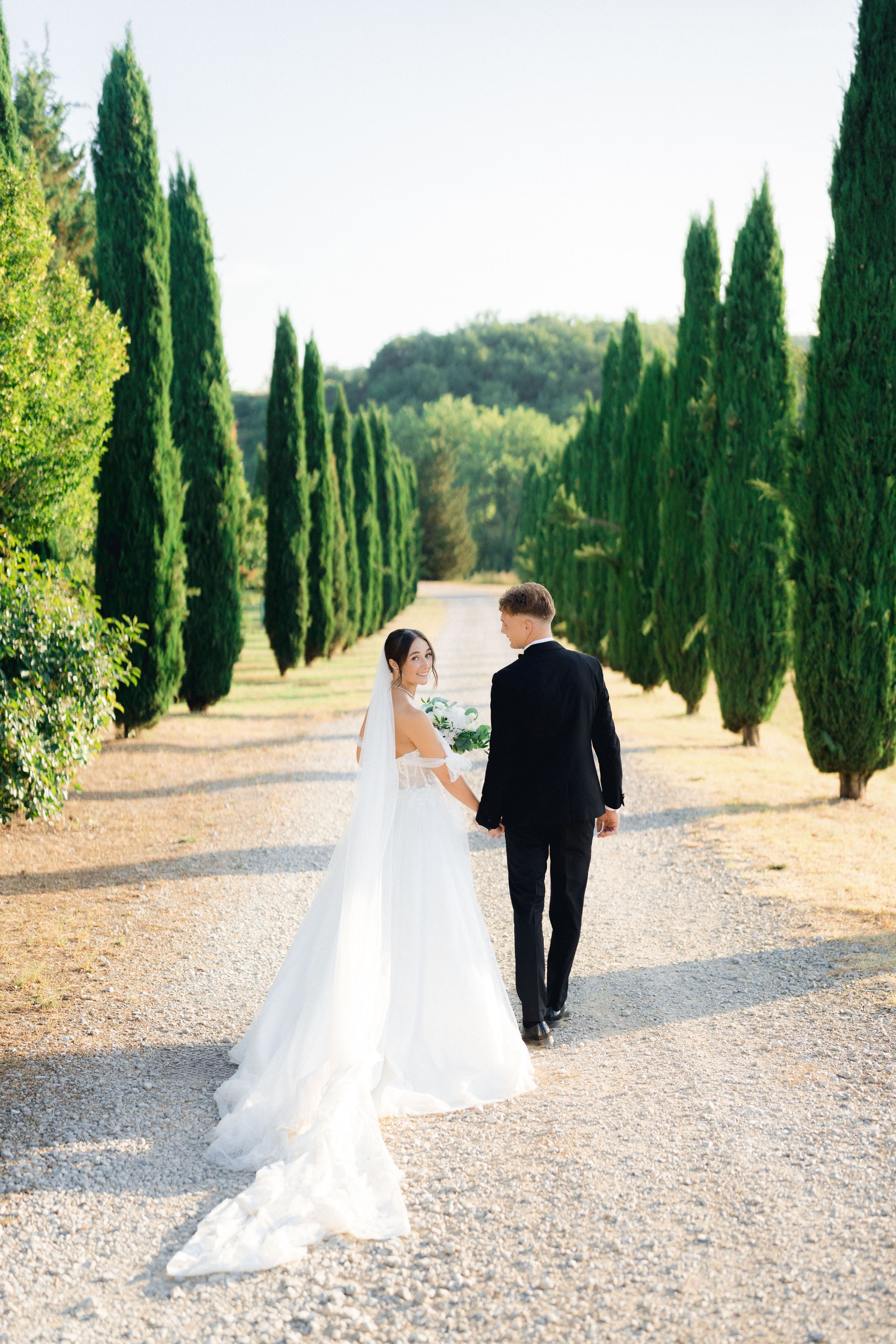 Bride and groom walking down a tree-lined road at their Italian destination wedding