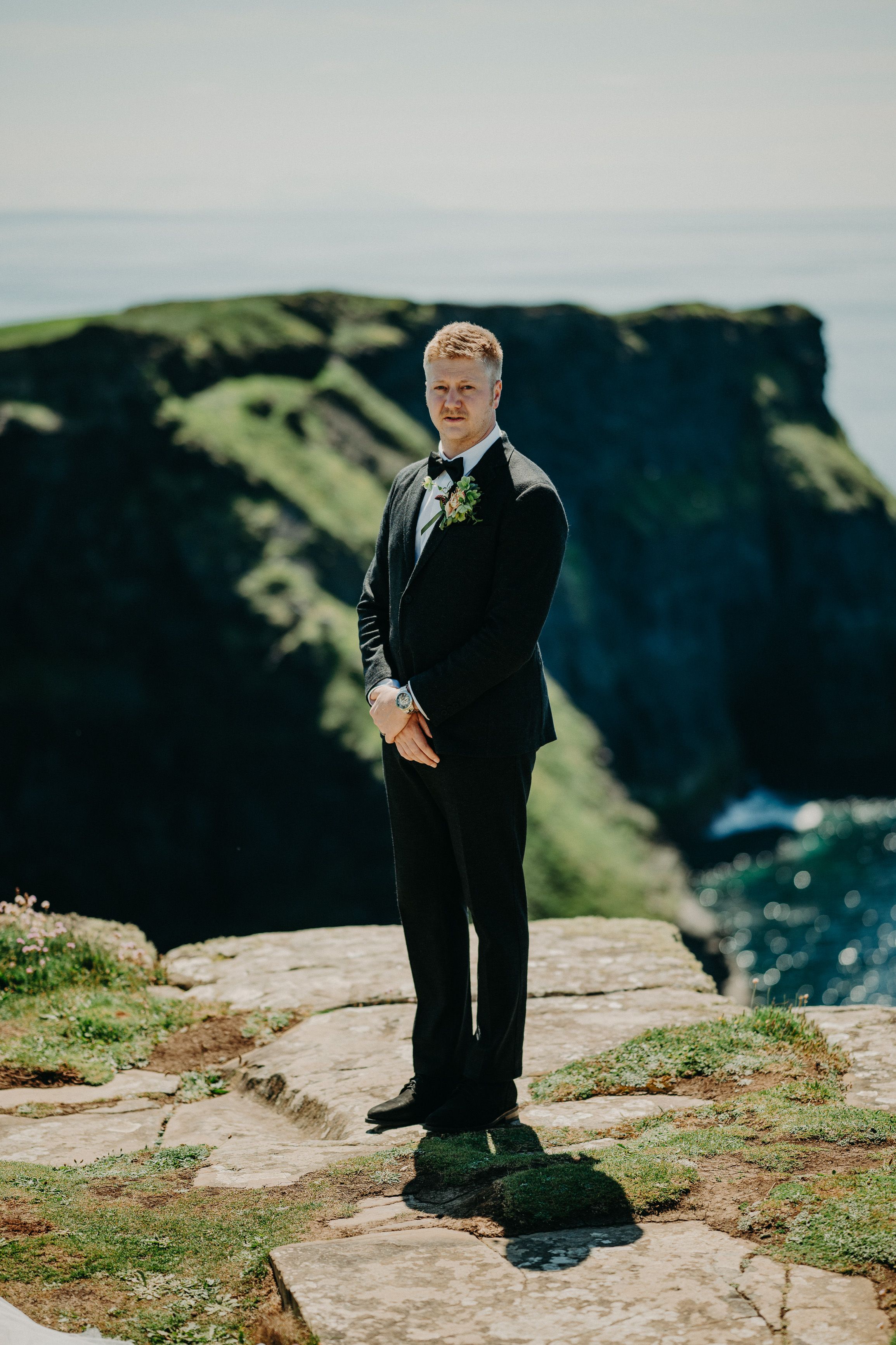 A groom standing on top of a cliff with amazing views of the sea during a small wedding in Ireland