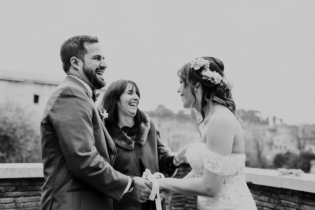 Bride and groom laughing with their celebrant during the ceremony of their elopement in Italy atop a Roman venue