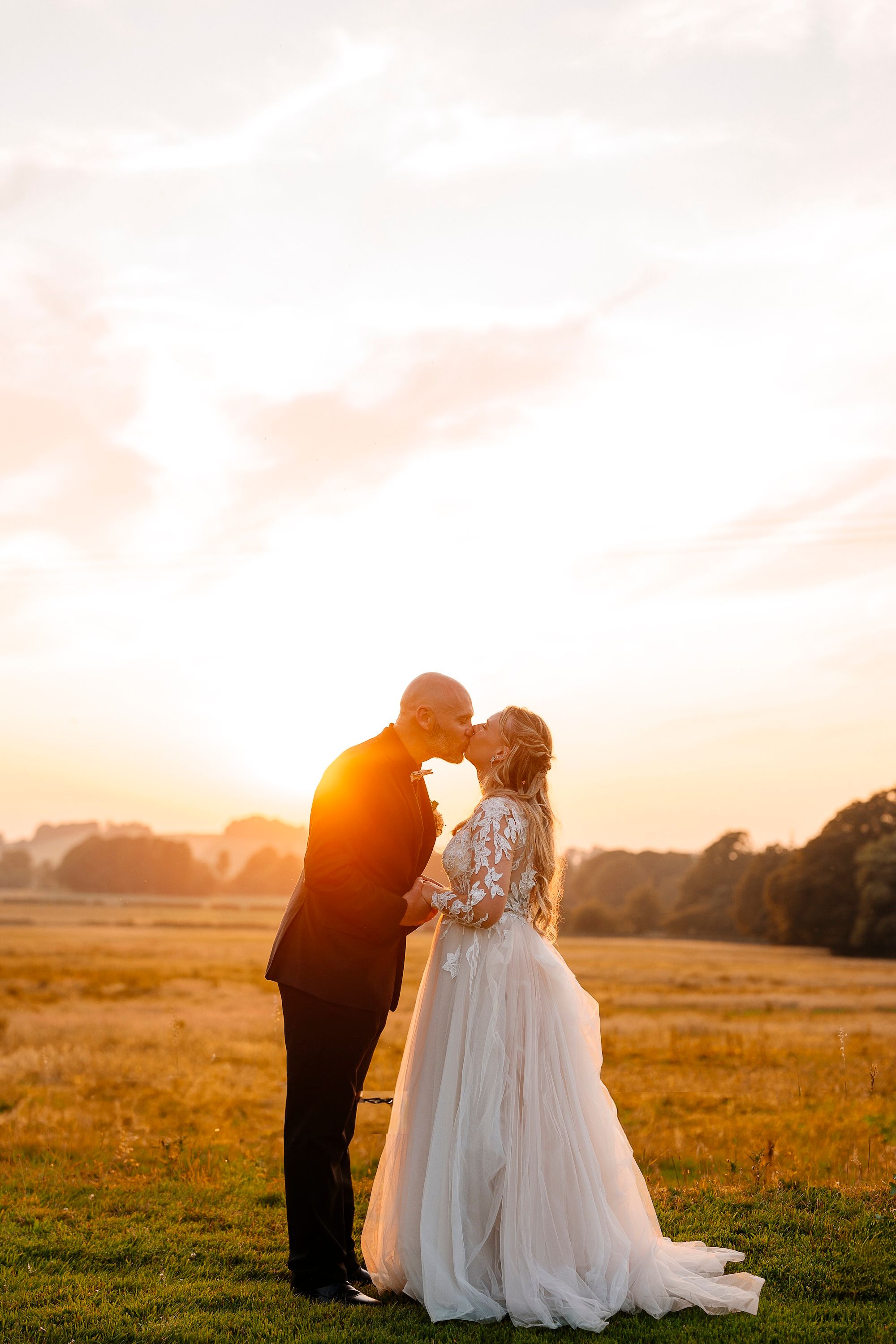 Newlyweds in a lush field kissing with the sunset in the background during the photoshoot of their micro wedding in Ireland