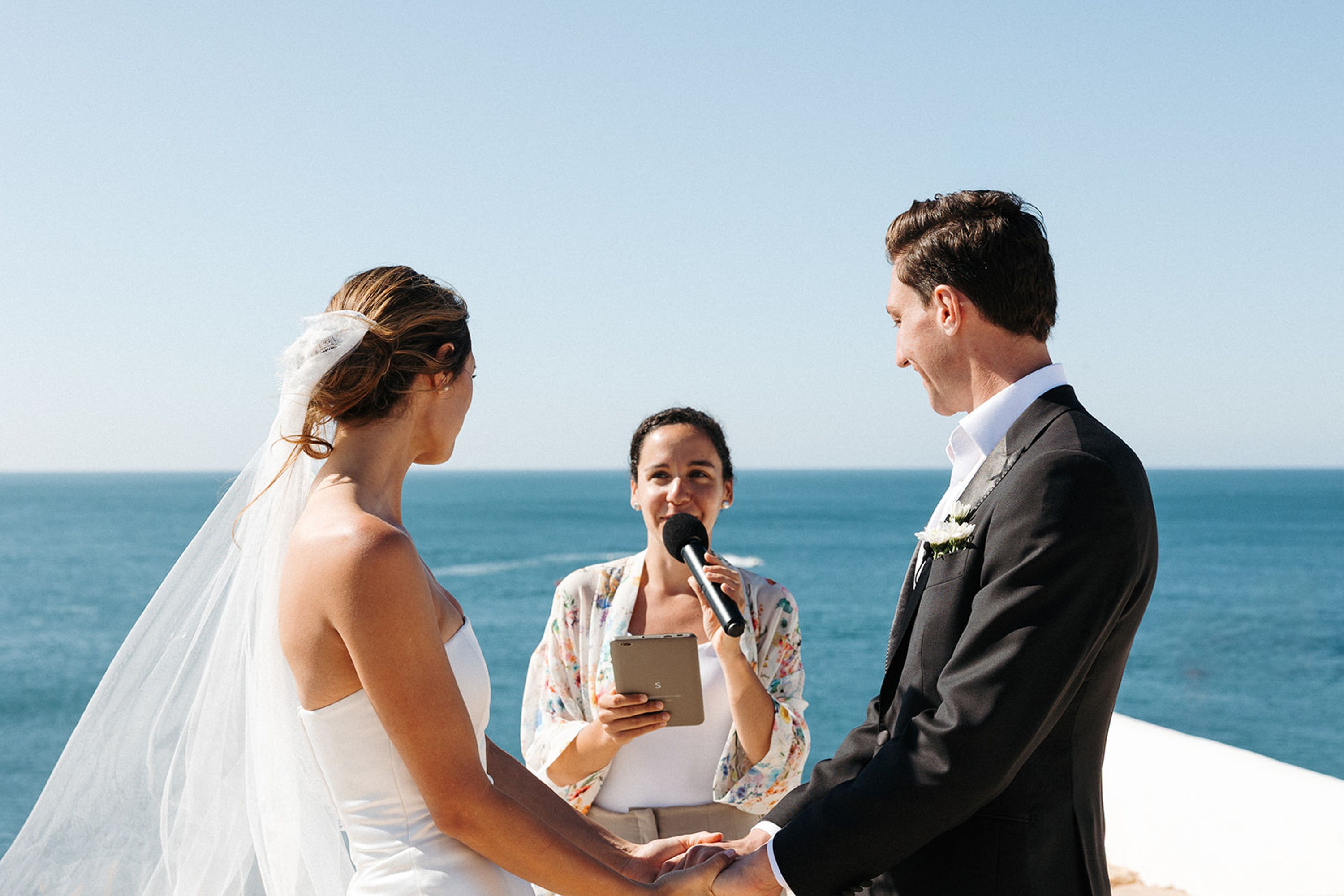 Bride and groom holding hands during a seaside ceremony at a small wedding in Portugal with ocean backdrop