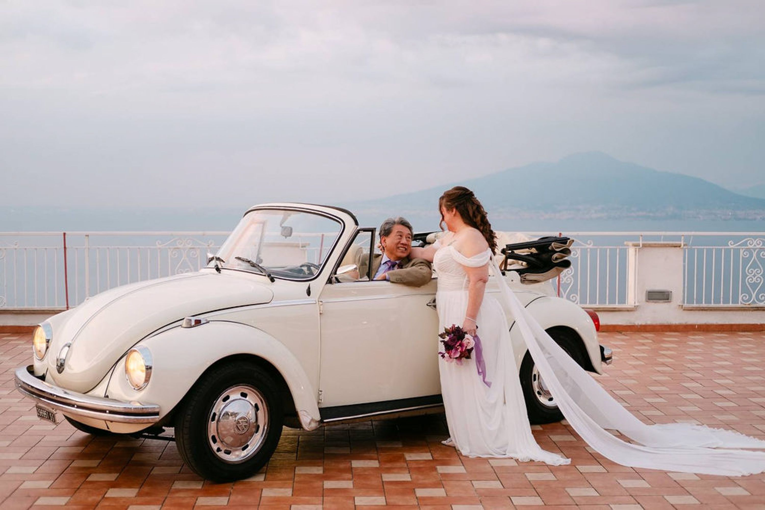 Bride smiles at groom seated in a classic convertible during a small wedding in Italy
