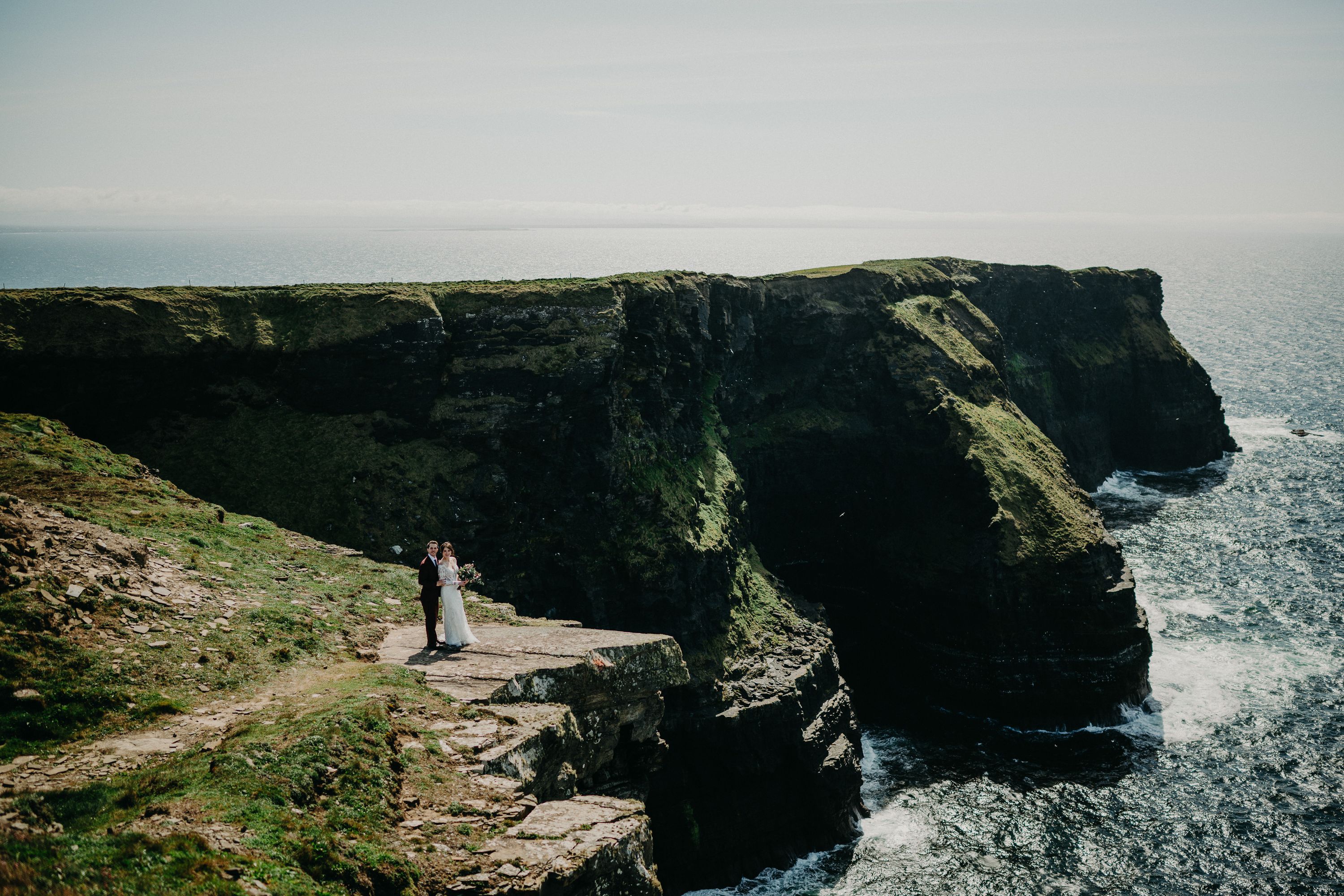 A bride and groom on top of a cliff beside the sea after their small wedding in Ireland