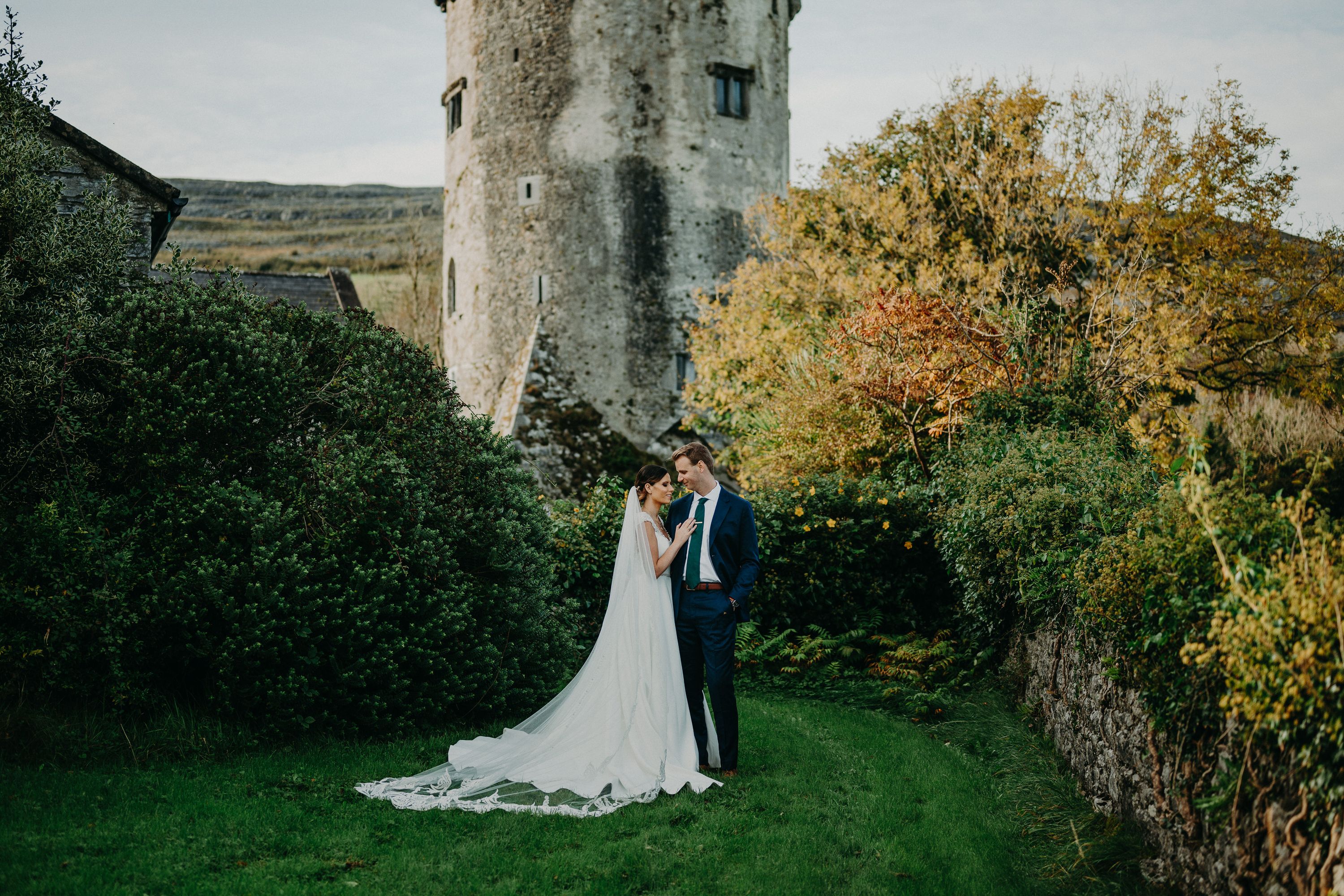 Bride and groom embracing in a castle garden with a historic tower backdrop at an intimate wedding in Ireland.