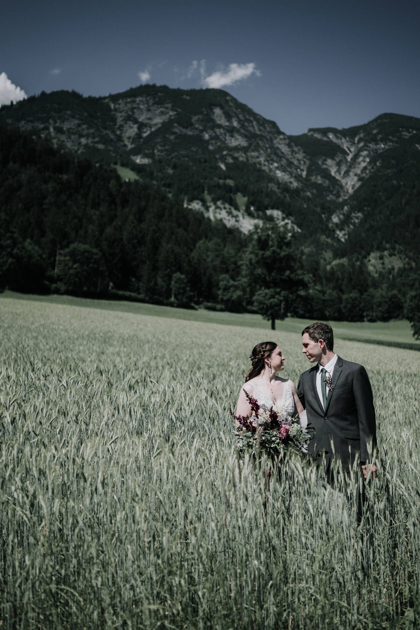 Bride and groom standing in a green field beneath the Austrian Alps