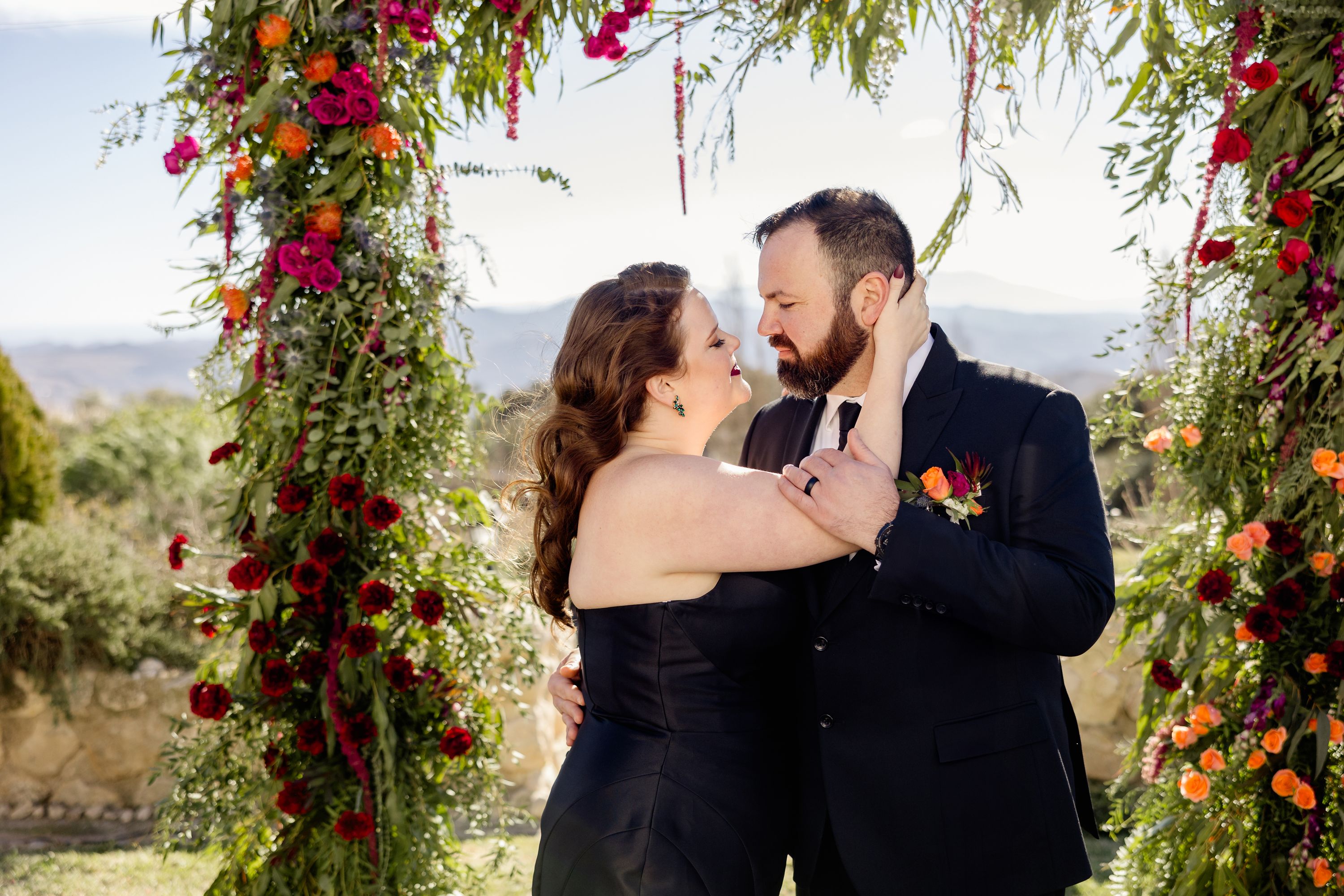 Bride and groom in back holding each other in a small wedding in Spain with floral arch in the background