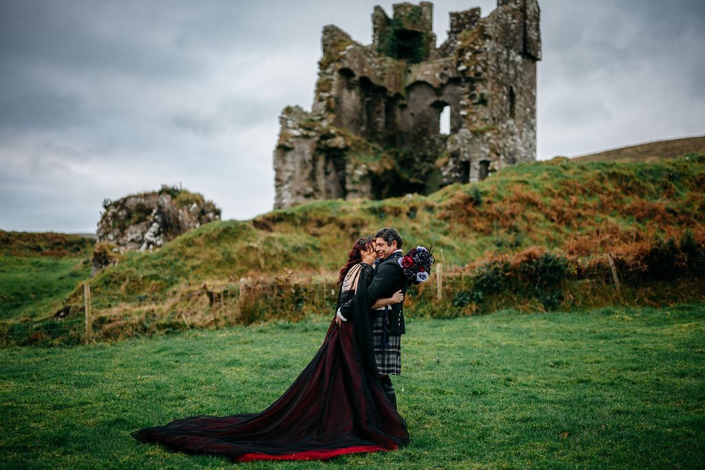 Bride and groom kiss in wide open meadows, with a castle ruin in the background during the photoshoot of their elopement in Ireland