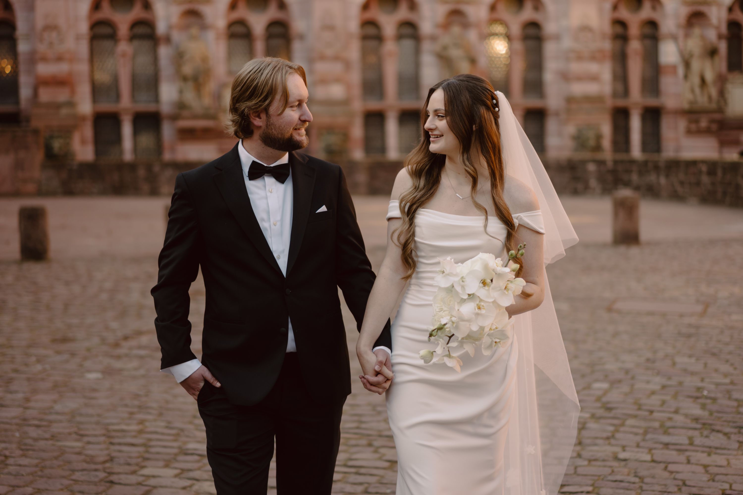 Newlyweds smiling while walking on a brick road with a castle in the background in Germany