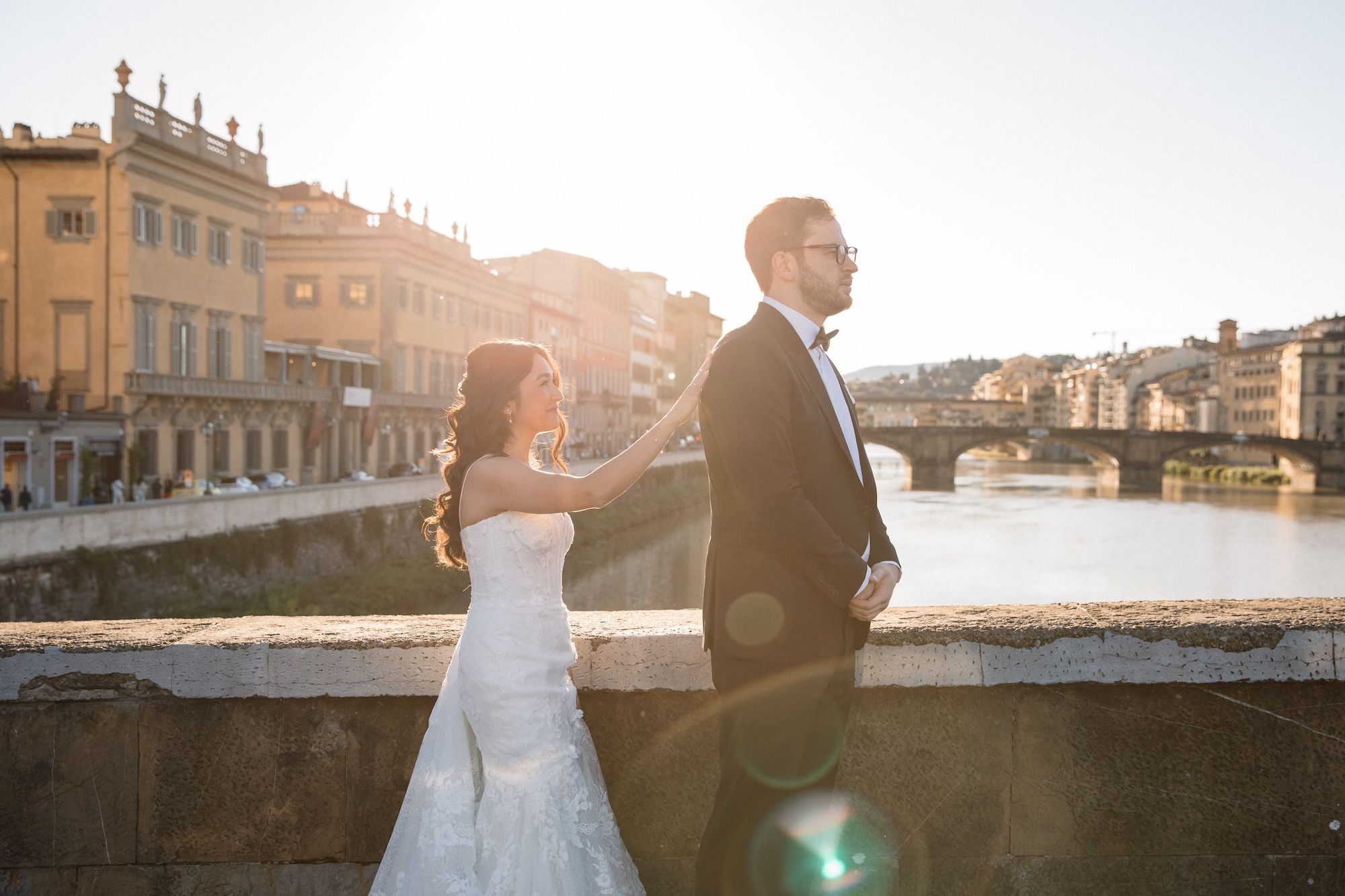 Bride tapping her groom on the shoulder in a bridge over Florence, during the first look of their vow renewal in Italy