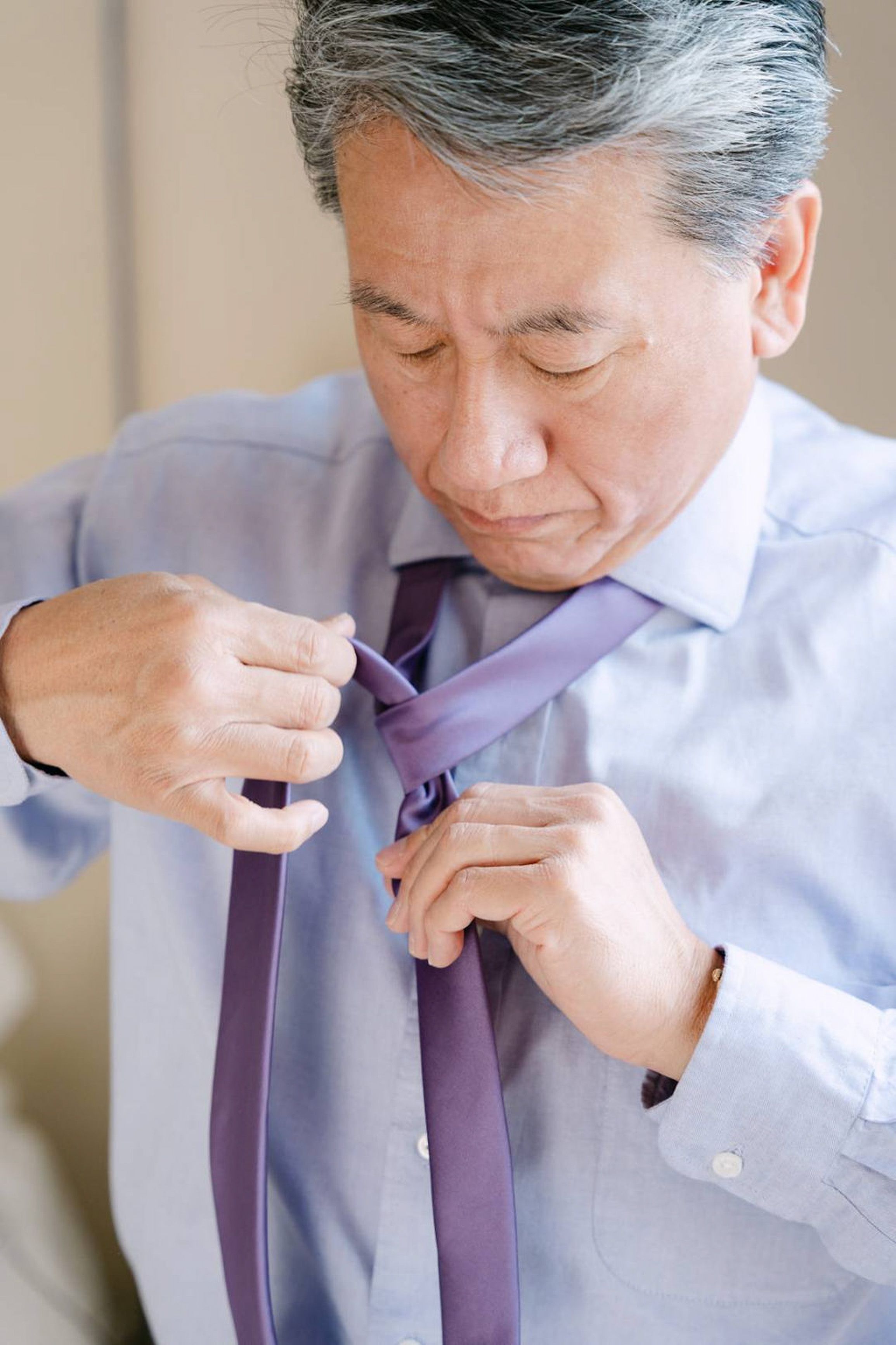 Groom tying a lavender necktie while getting ready for a small wedding in Italy